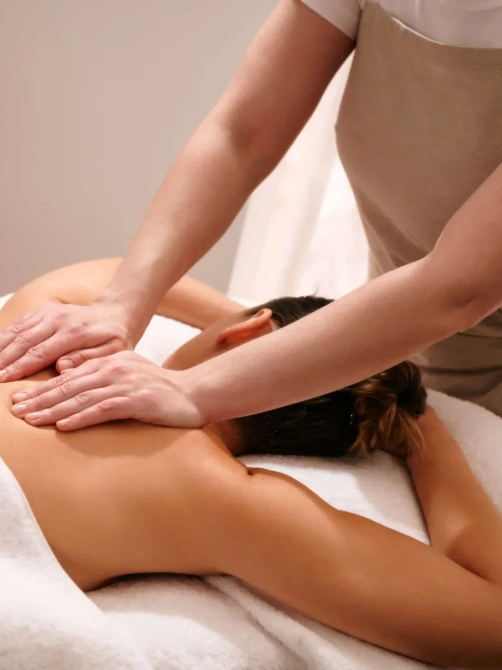 Massage therapist performing a relaxing back massage on a client lying face down on a treatment bed.