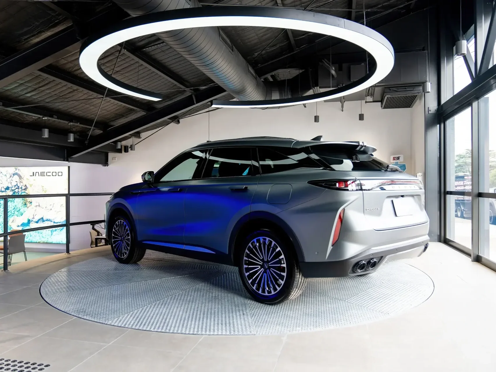 an omoda jaecoo silver car on a rotating platform under a spotlight