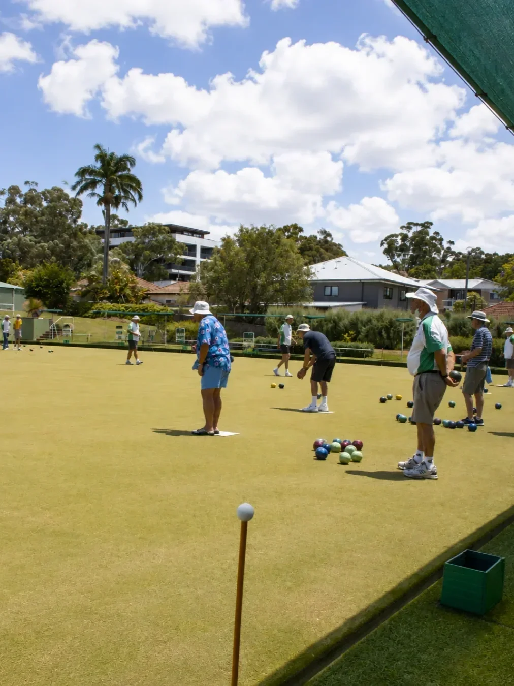 People playing lawn bowls on a sunny day at Gymea Bowling Club, with bowls scattered across the green.