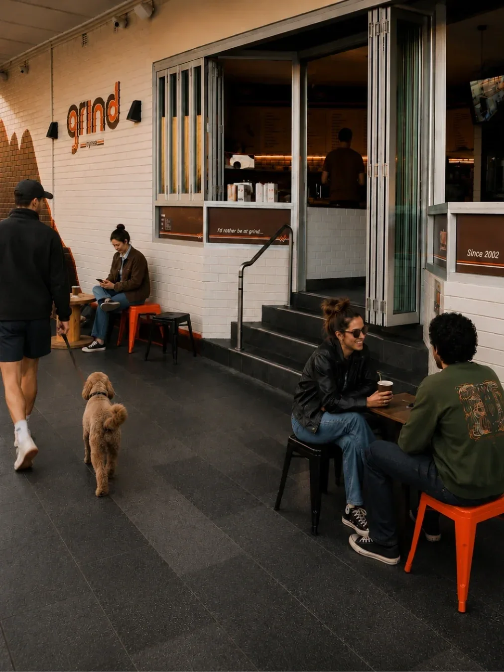 Street view of Grind café in Gymea, with customers seated outside, a dog passing by and the café’s open frontage in the background.