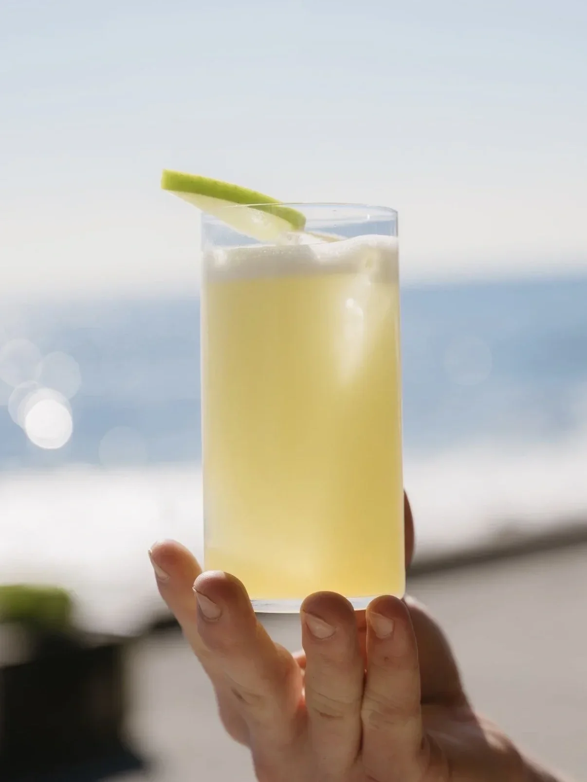 meadows adams apple cocktail held up in front of the beach