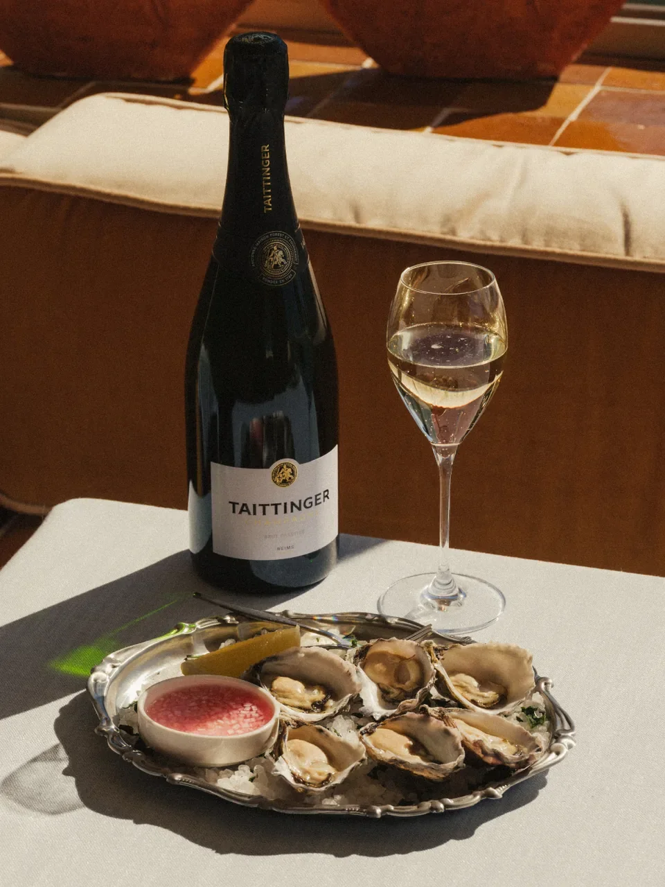 Bottle of Taittinger Champagne and a glass beside a plate of fresh oysters with lemon and a dipping sauce at Summer Salt in Cronulla.