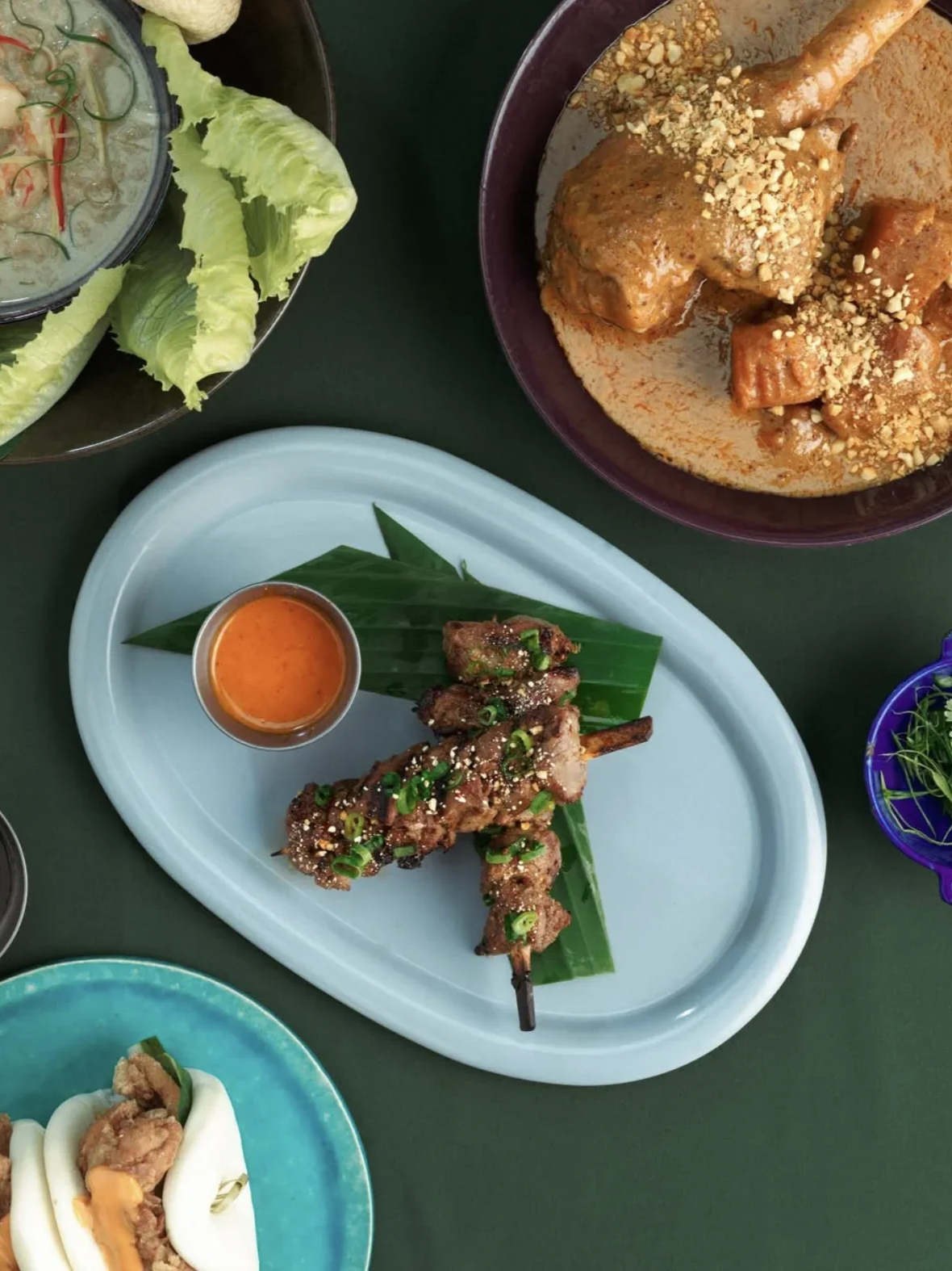 A peanut-topped curry, skewered grilled meat and lettuce cups arranged on a shared dining table.