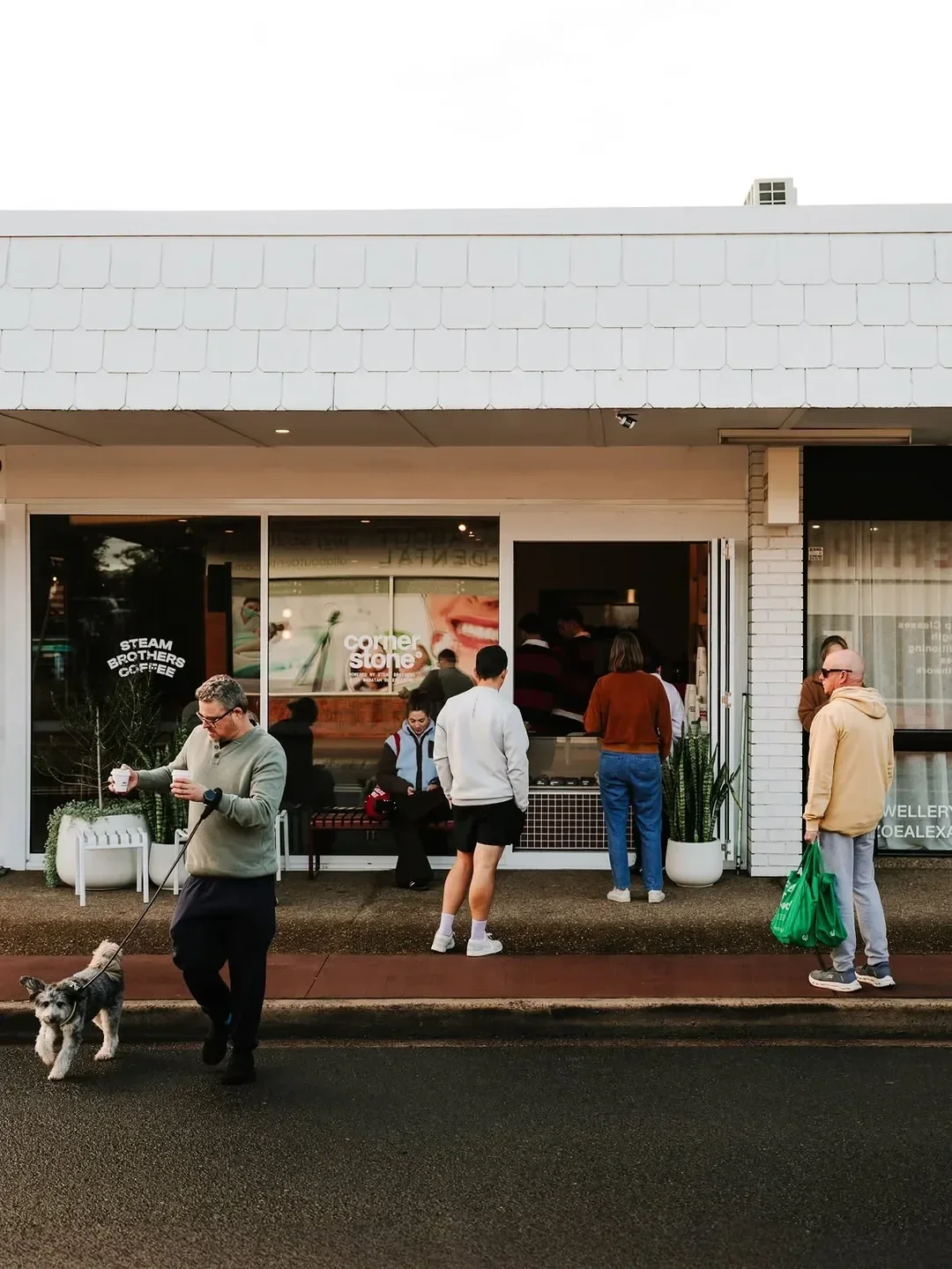 Customers gathered outside Cornerstone café in Engadine, with a man walking his dog in the foreground.