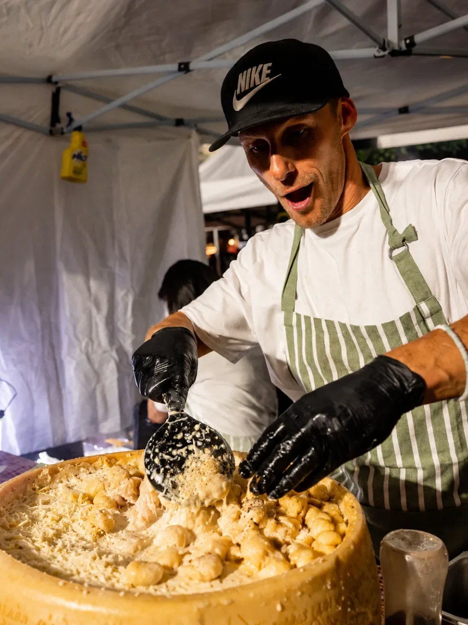 Chef scooping gnocchi from a large cheese wheel at an Eat Drinks Nights stall in Engadine.