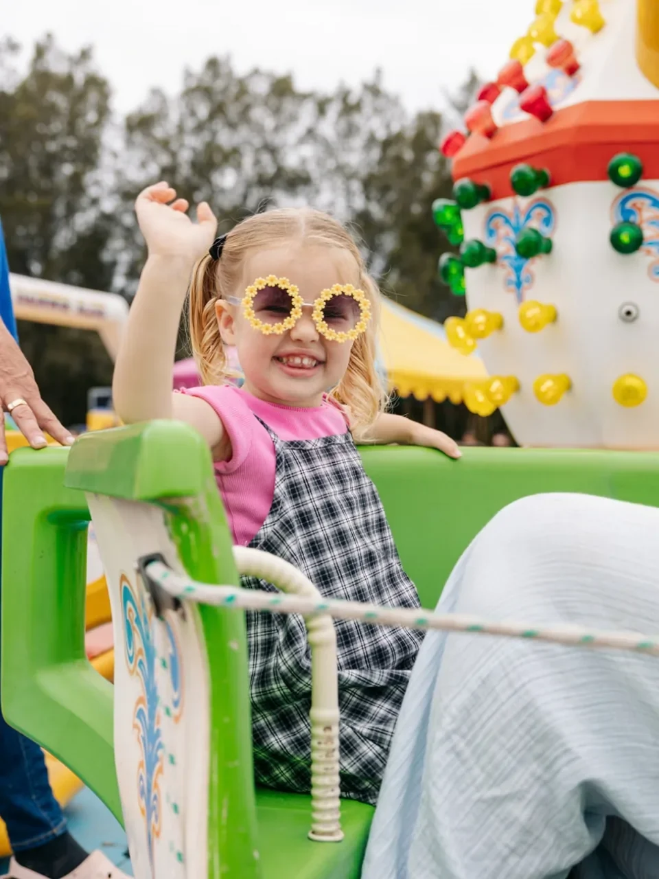 Young girl in flower-shaped sunglasses waving from a carnival ride at Kurnell Village Festival.