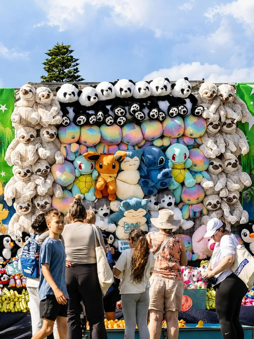 A CronullaFest showbag stall stacked with plush toys — pandas, sloths and colourful character animals — with families browsing the sideshow alley display.