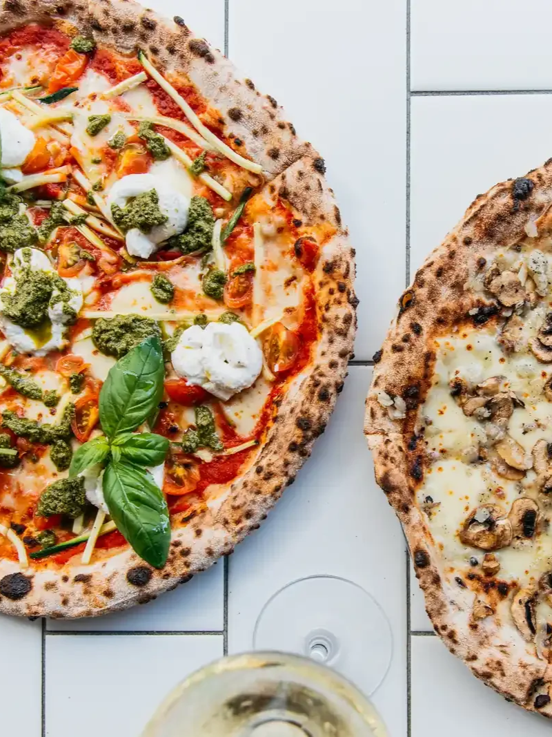 Two wood-fired pizzas side by side, one topped with tomato, bocconcini and basil, the other with mushroom.