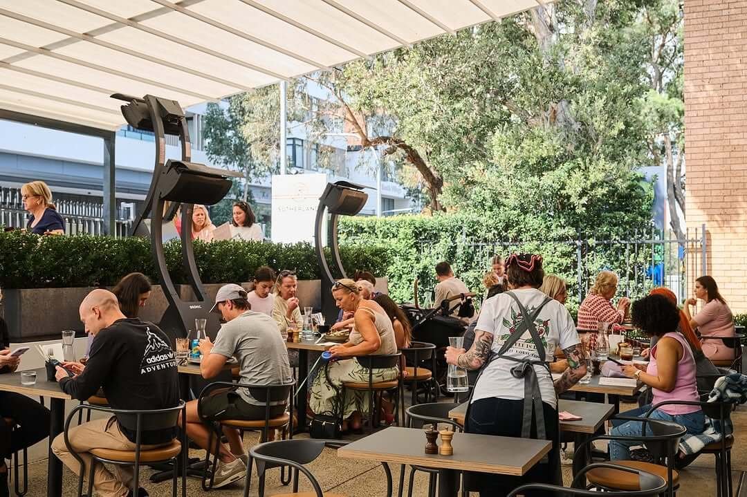 customers dining at an undercover outdoor cafe with black tables and overhead heaters