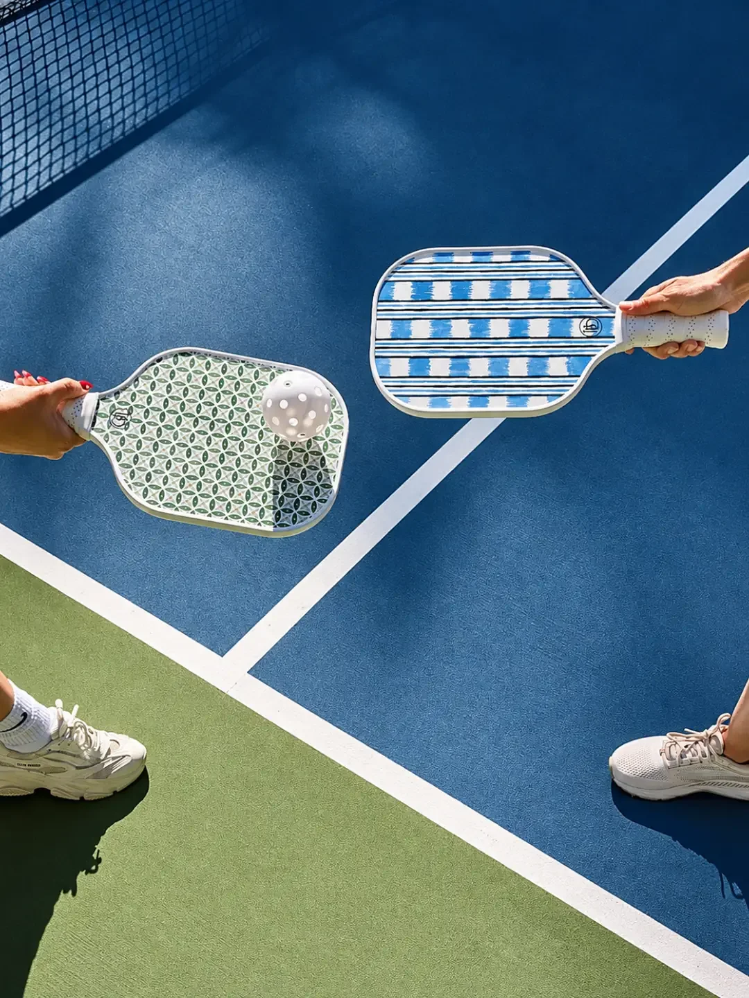 Two players hold patterned paddles and a ball above a blue and green court at Picklr in Cronulla.