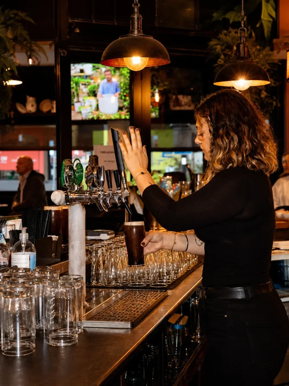 Bartender pouring a beer from the tap behind the bar at Snug Bar in Gymea, surrounded by warm pendant lighting and glassware.