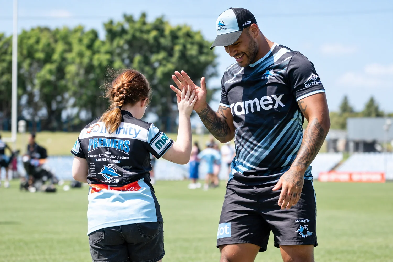 A Cronulla Sharks player high-fives a young fan in a Sharks 2016 premiers jersey on the field during a school holiday program.