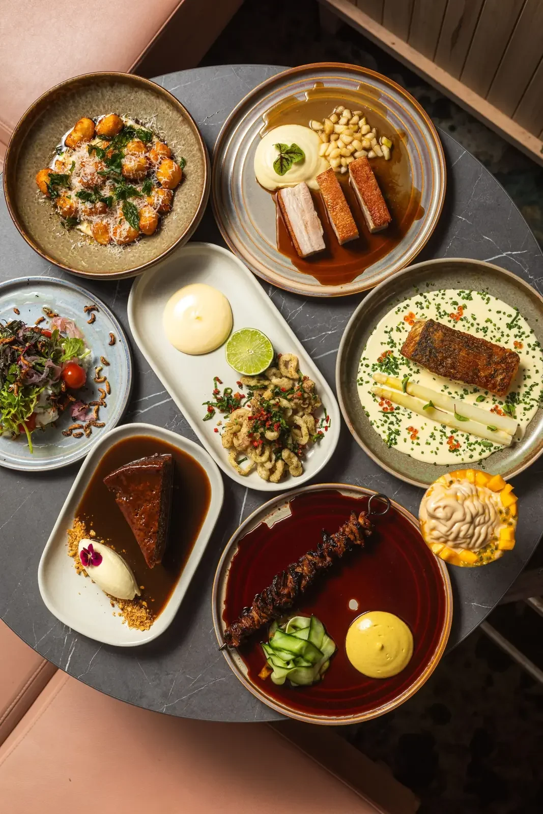 An overhead spread of shared dishes including gnocchi, pork belly, salmon with asparagus, a sticky date pudding and a mango dessert.