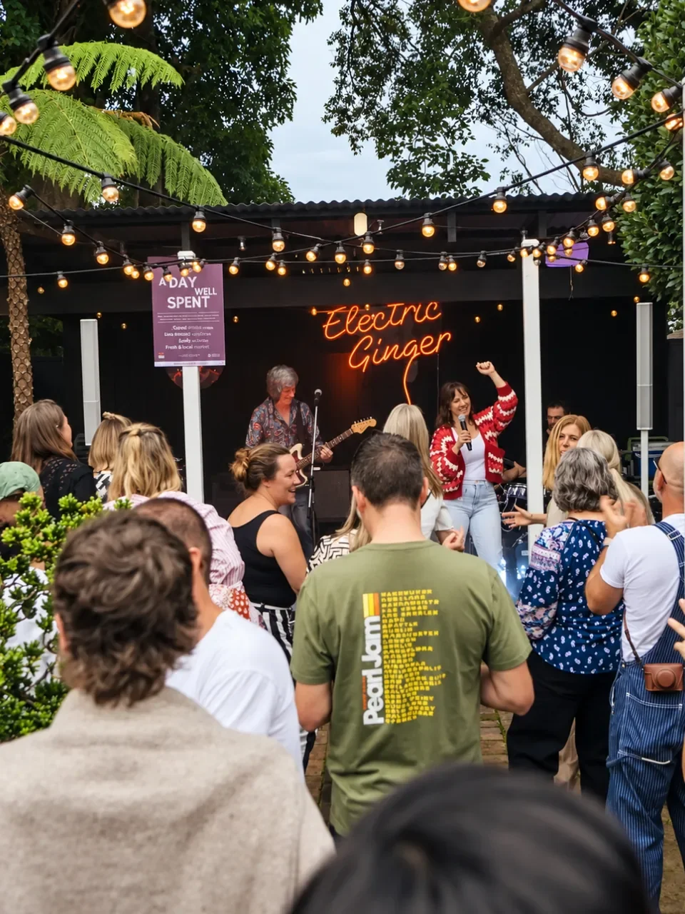 Crowd watching a band play beneath an "Electric Ginger" neon sign in a festoon-lit courtyard at Berry Folk in Berry.