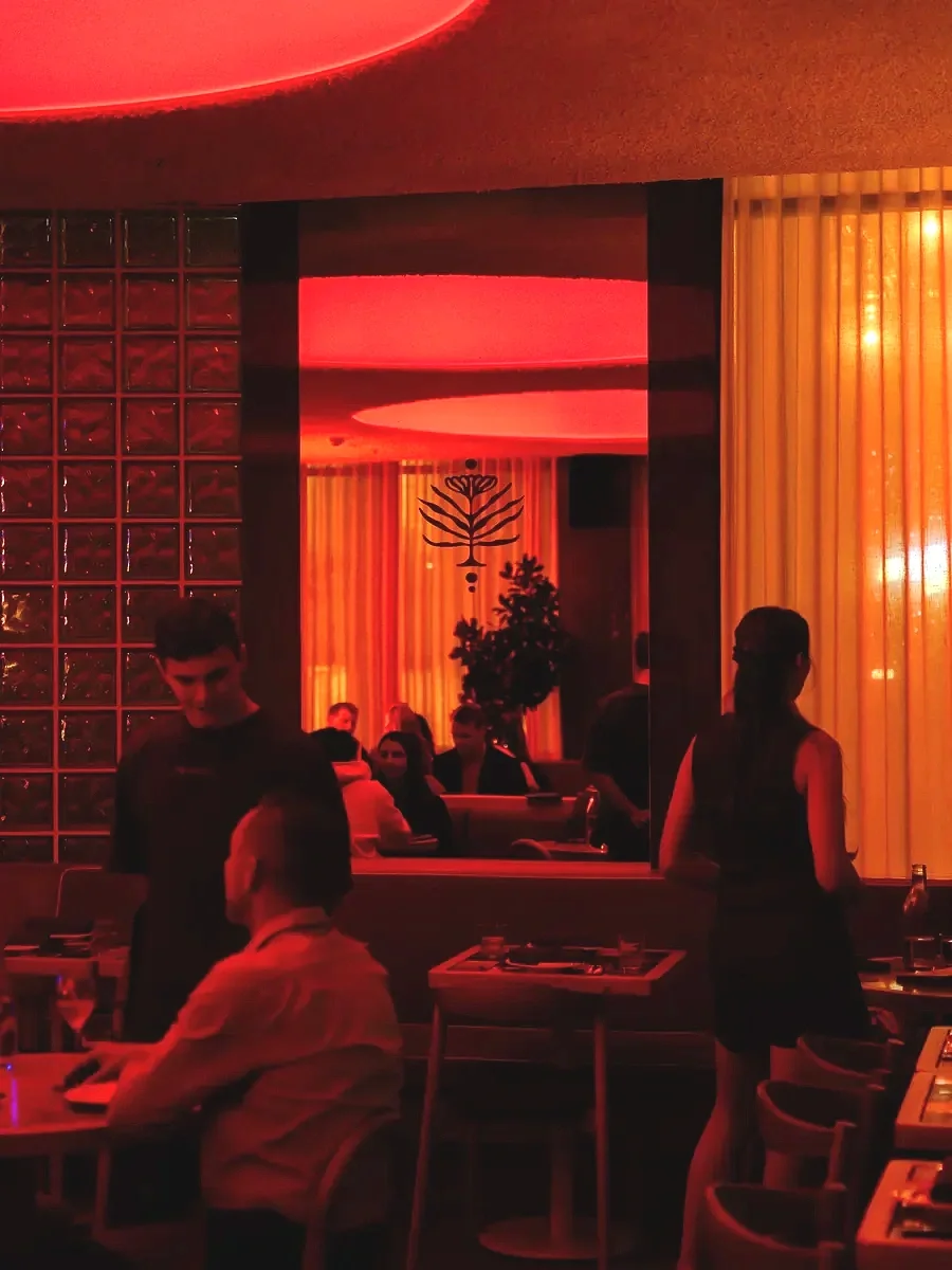 Interior of Meadow in Cronulla, featuring moody red lighting, glass brick walls, warm illuminated curtains and guests dining in the intimate restaurant and bar.