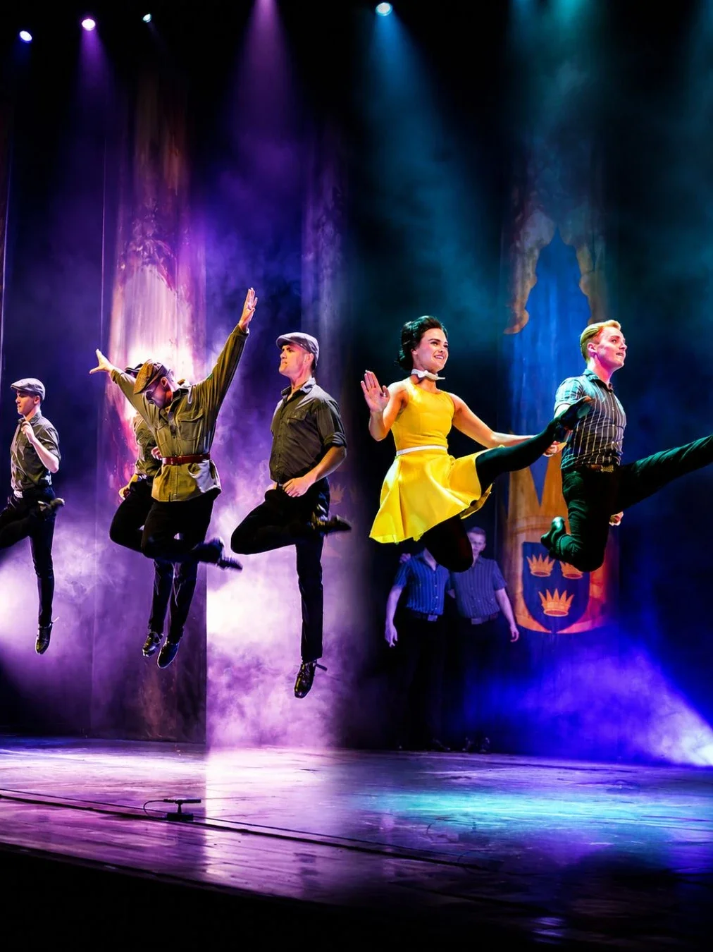 Dancers from A Taste of Ireland mid-leap on a smoky, spotlit stage, with a performer in a yellow dress and others in vintage-style costumes in front of a crest backdrop.