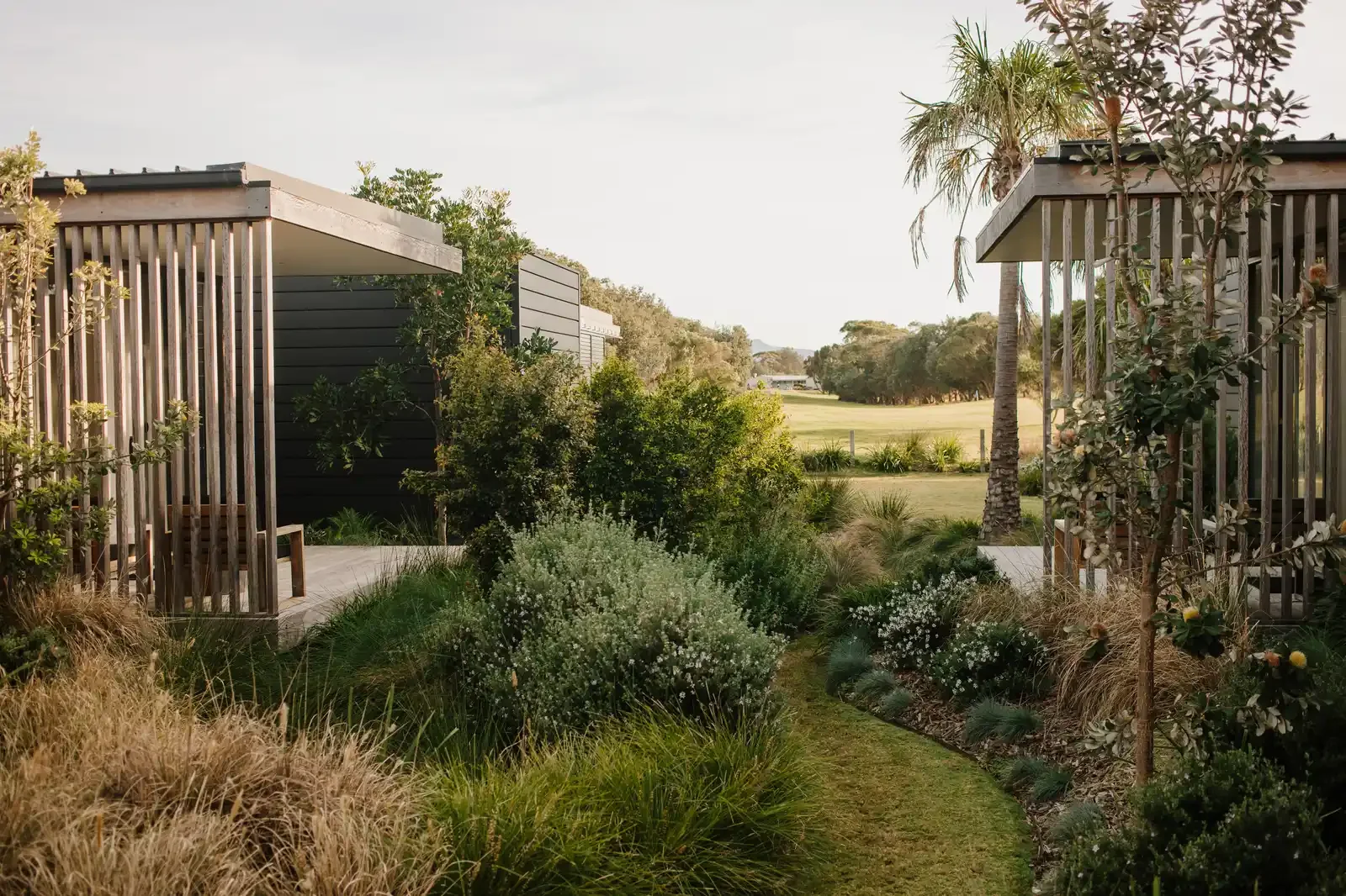 Timber lounge chairs set on a grassed deck area, overlooking open green paddocks and a rustic wooden fence line.