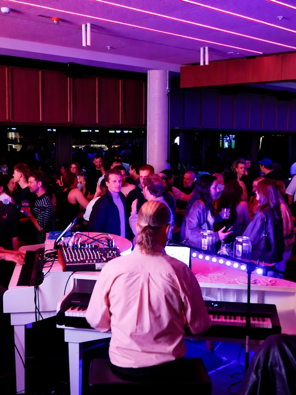 Crowd gathered around two white pianos under pink lighting at a live music night at Social House in Cronulla.