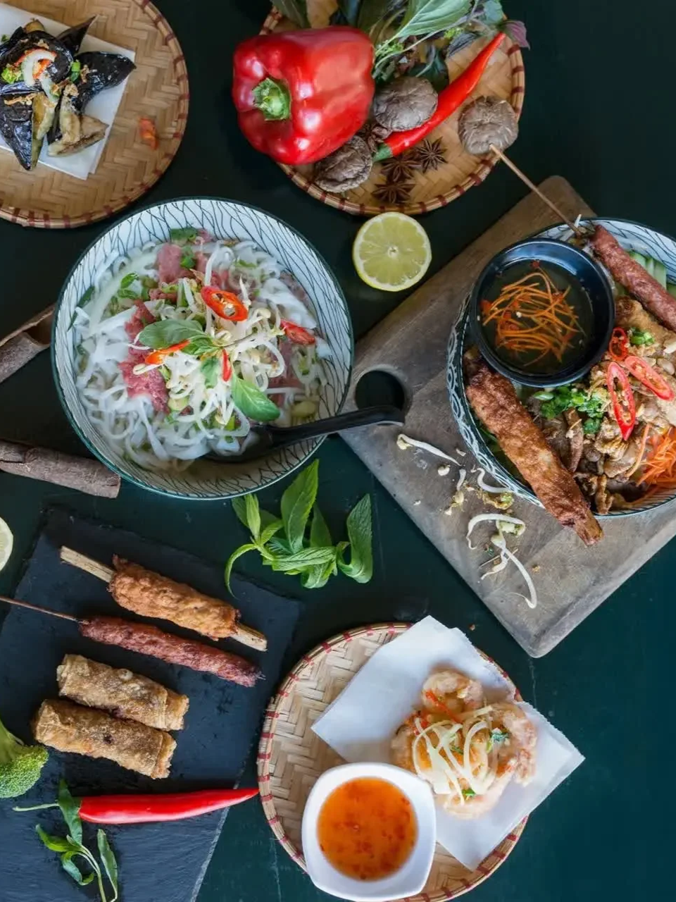 A Vietnamese share table with a bowl of pho, spring rolls, skewers and fried dishes.