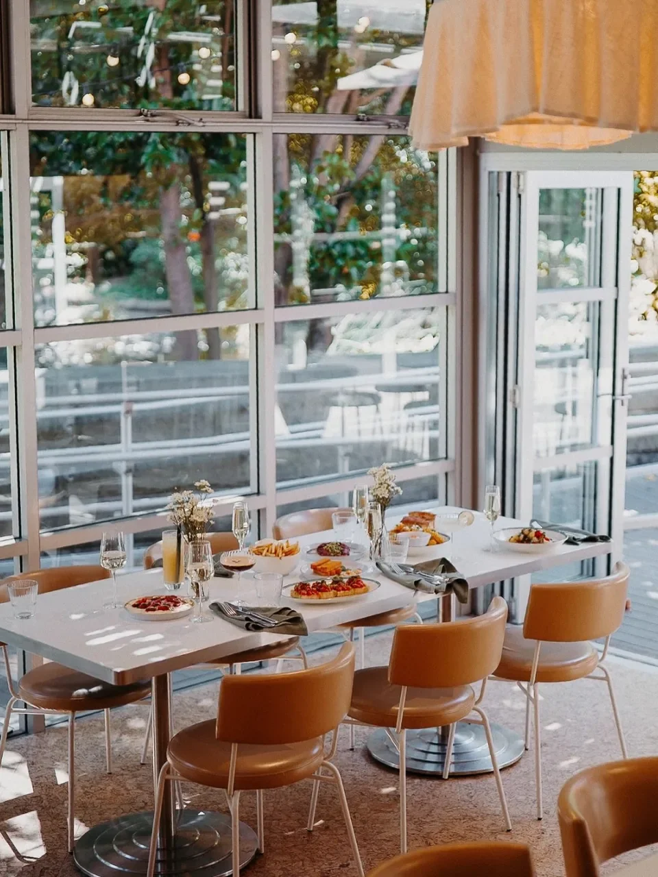 Light-filled dining room at Hazel in Gymea with tan leather chairs and a table of shared plates beside tall windows.