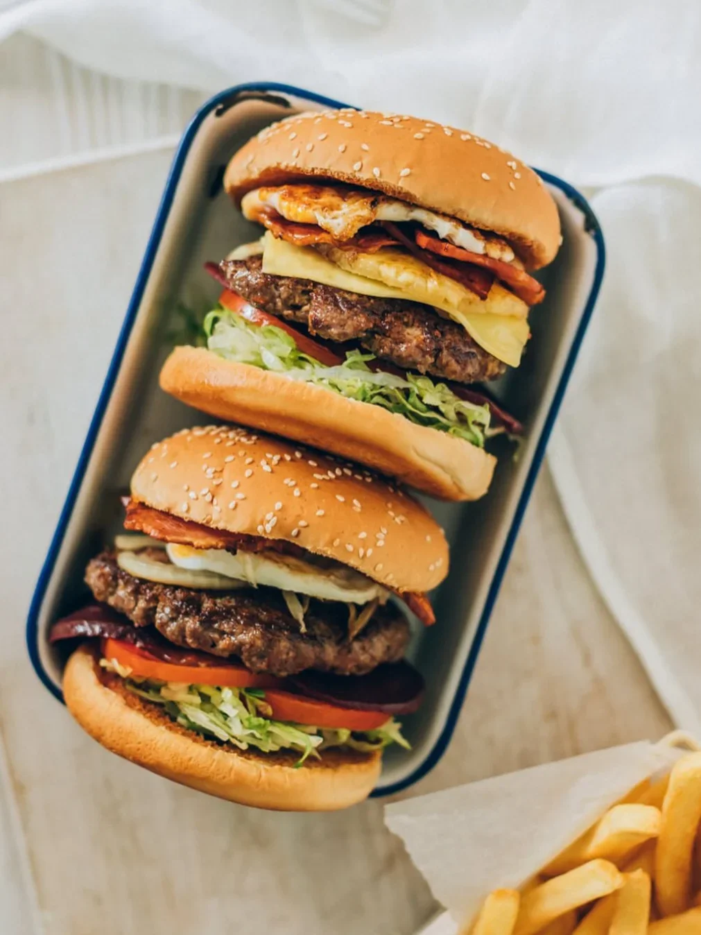 Two burgers with beef patties, fried egg, bacon and salad in an enamel tray, served with chips at Grills on Wills.