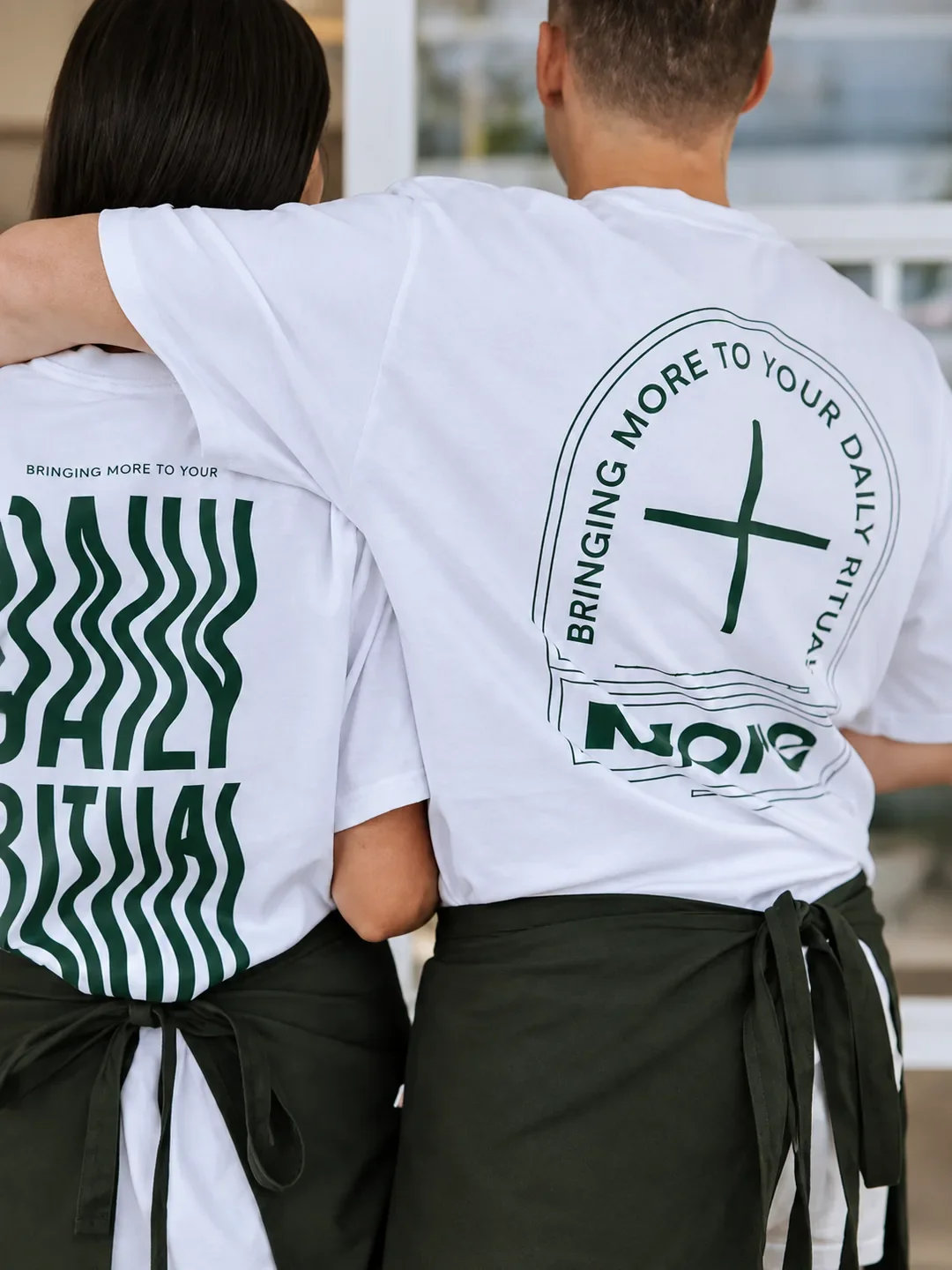 Two staff in white T-shirts and green aprons printed with "Bringing more to your daily ritual" at More Daily Ritual in Caringbah.