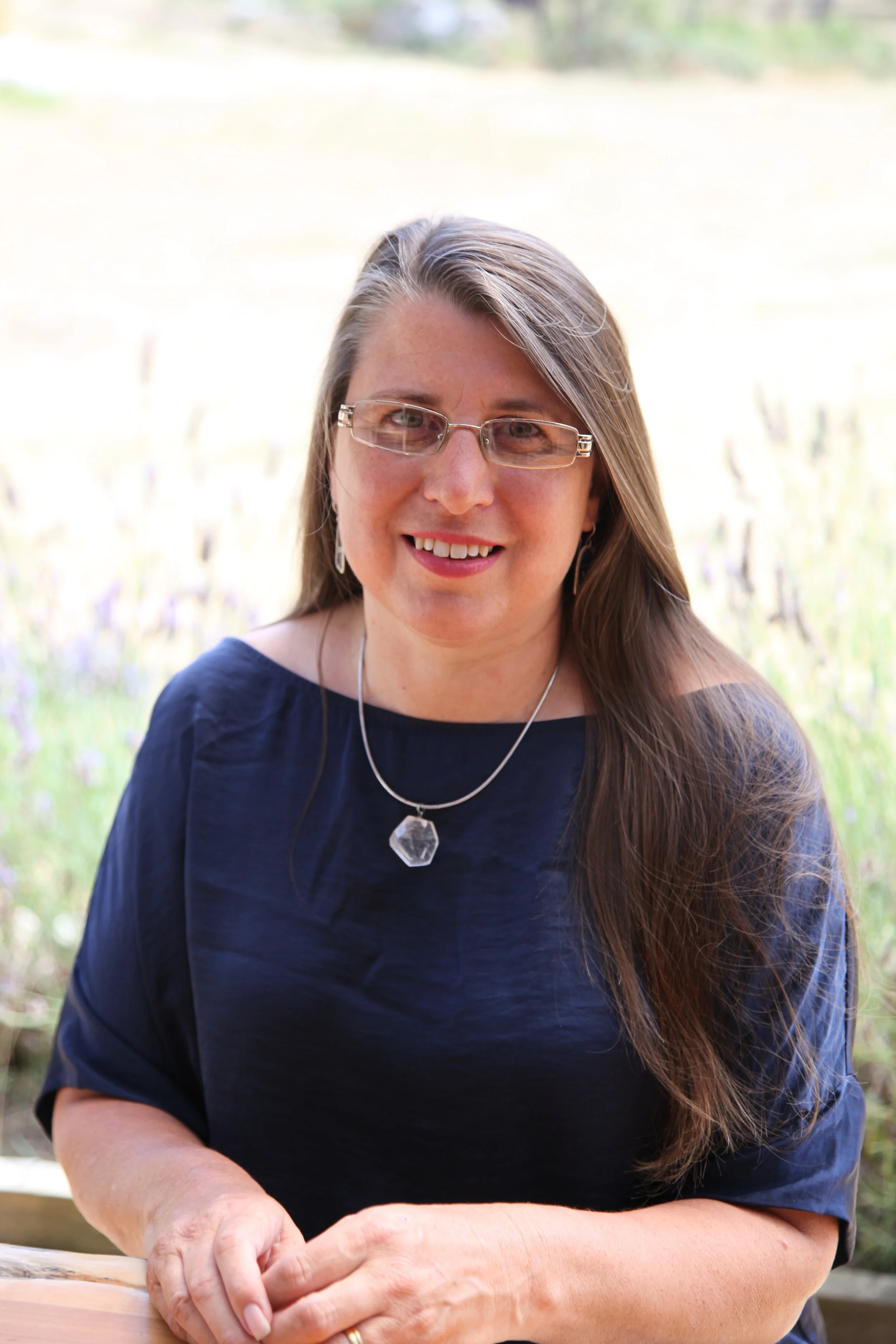 Amanda Erskine - sitting outside at a table on a sunny day with her flowing long hair - Money Energy intuitive Money Energy Healing practitioner