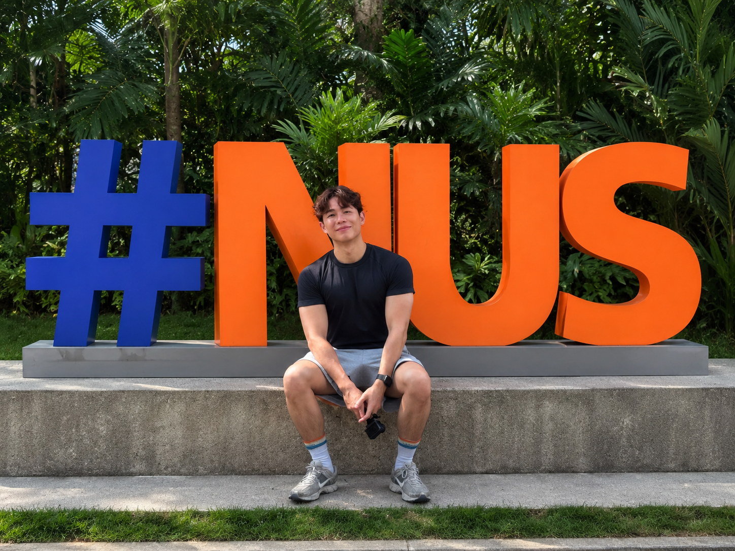 Sixmoredays Founder and Director Isaac Tng sitting in front of an NUS sign.