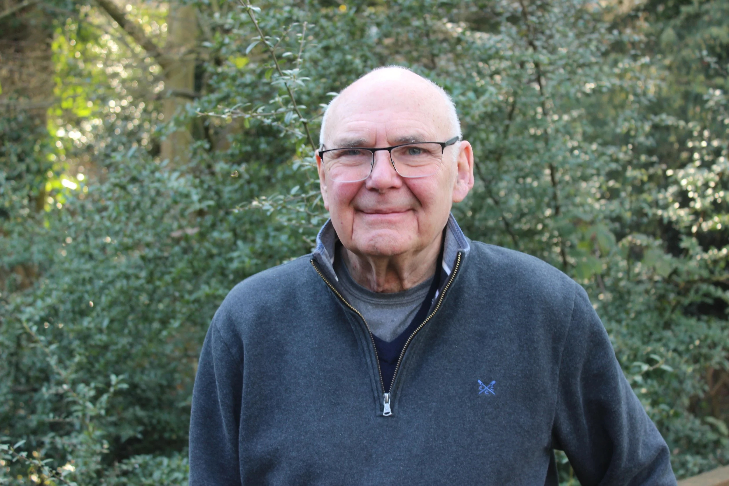 A man with glasses and a bald head smiling, holding a sign that reads 'Ron Jeeves Prophetic' in front of a stained glass window in a church or historic building.