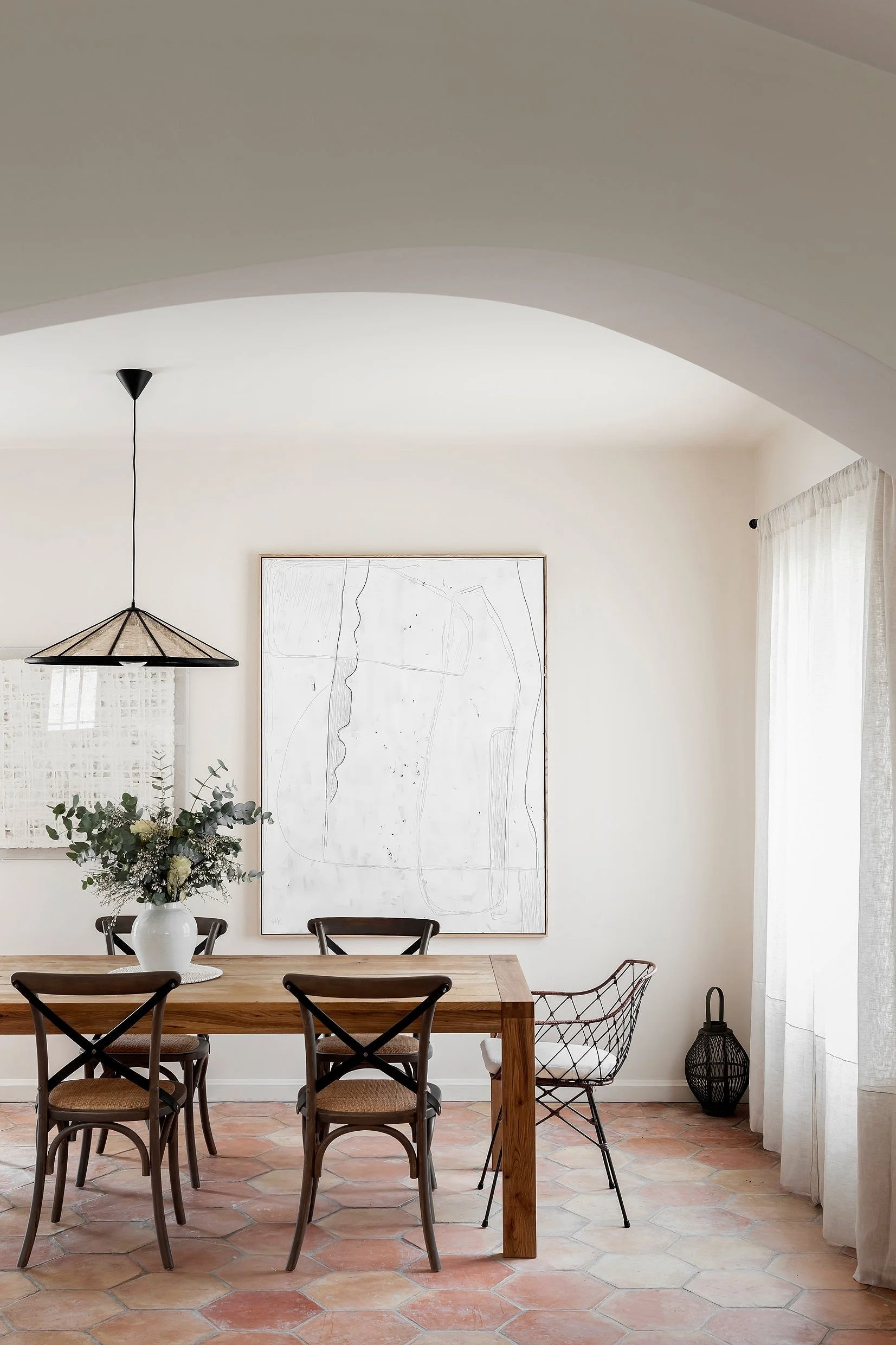 A dining room with a wooden table, four chairs, a vase with flowers, and a large abstract artwork on the wall.