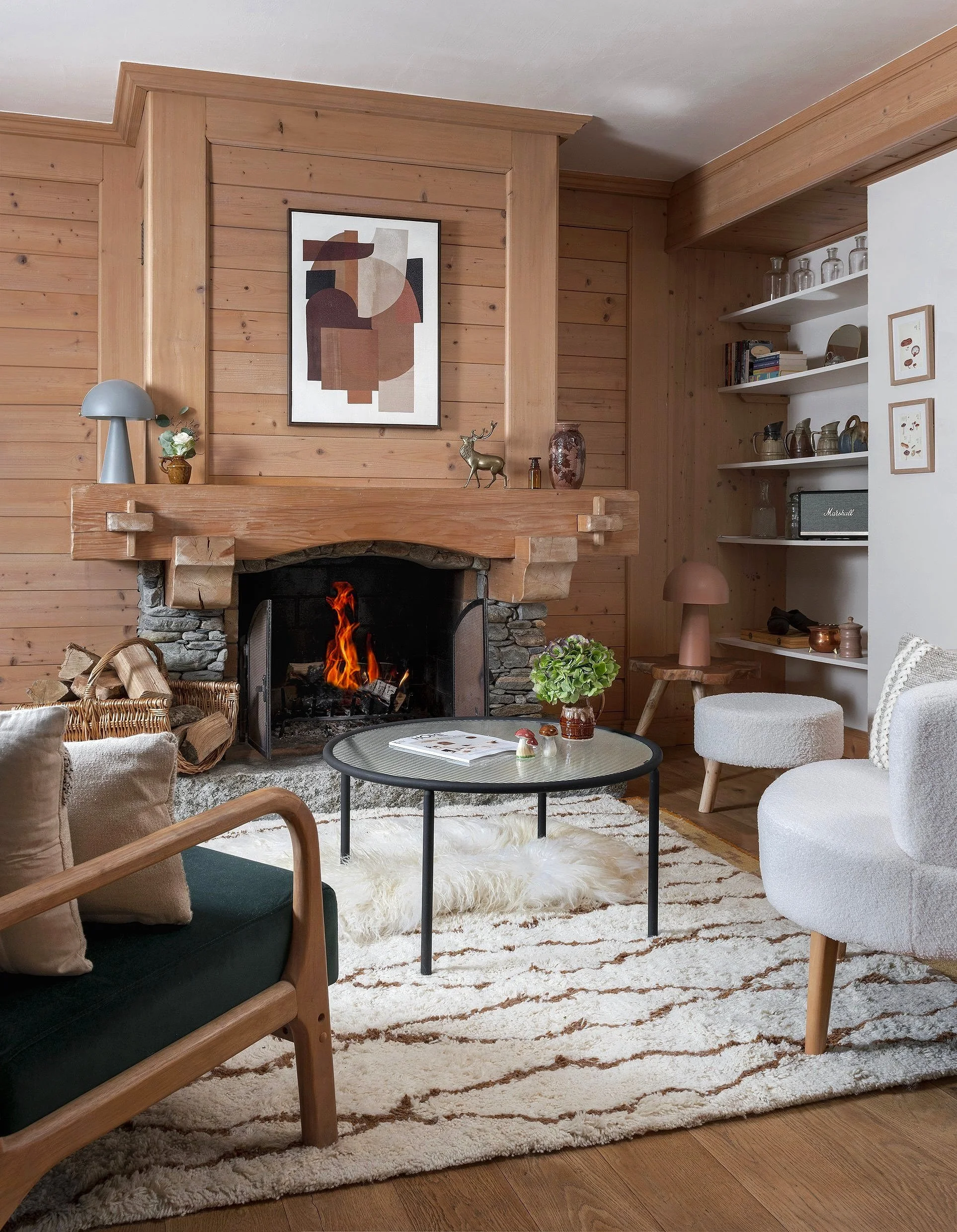 Living room with a stone fireplace, wooden walls, a round glass-top coffee table, white and beige seating, and decorative items.