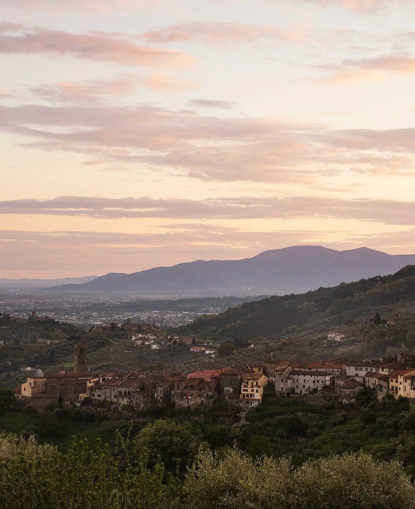 Scenic view of a hillside village at sunset with mountains in the background and a colorful sky.
