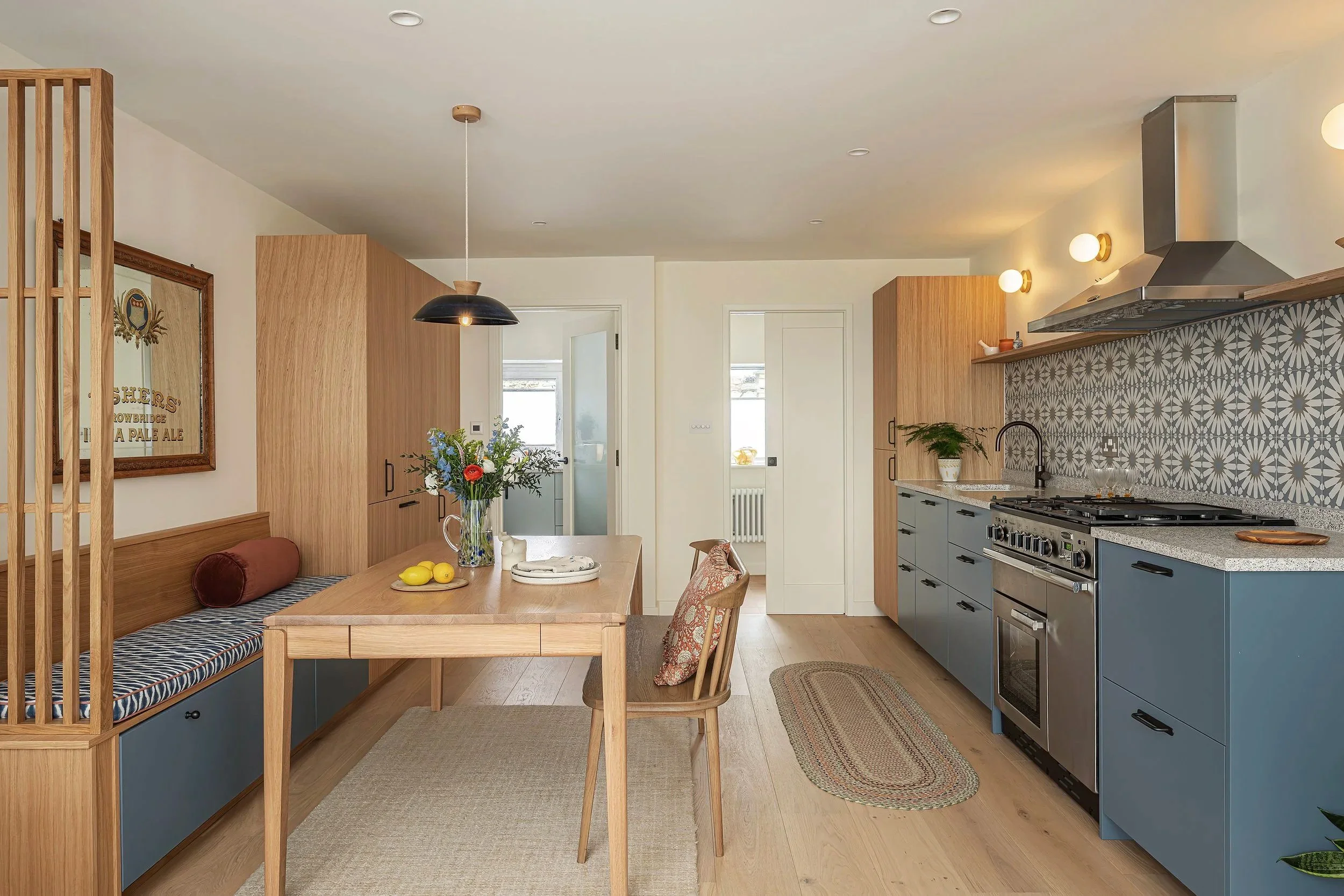 Modern kitchen and dining area with wooden accents, a patterned backsplash, and a table with a vase of flowers.