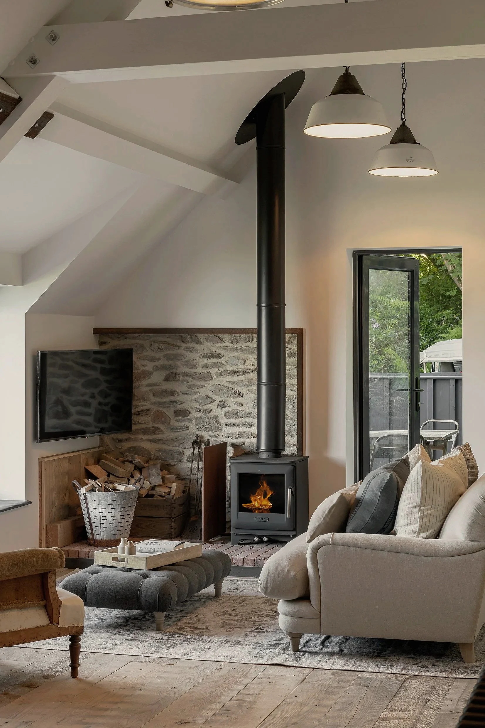 Living room with a wood stove, flat-screen TV, sofa with pillows, upholstered bench, and a sliding glass door leading to an outdoor space.