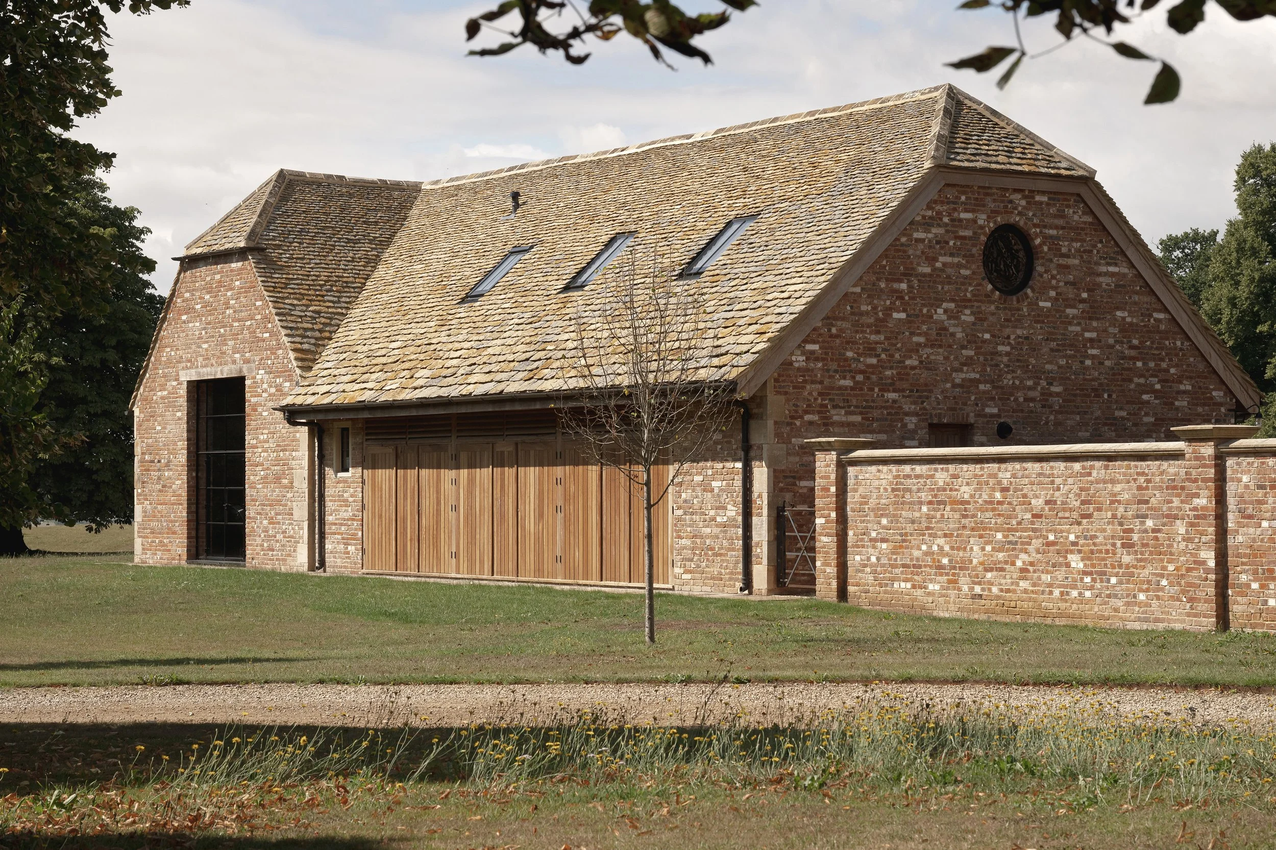 A brick house with a wooden garage door and a sloped roof with three skylights, surrounded by a lawn with a small tree in front.