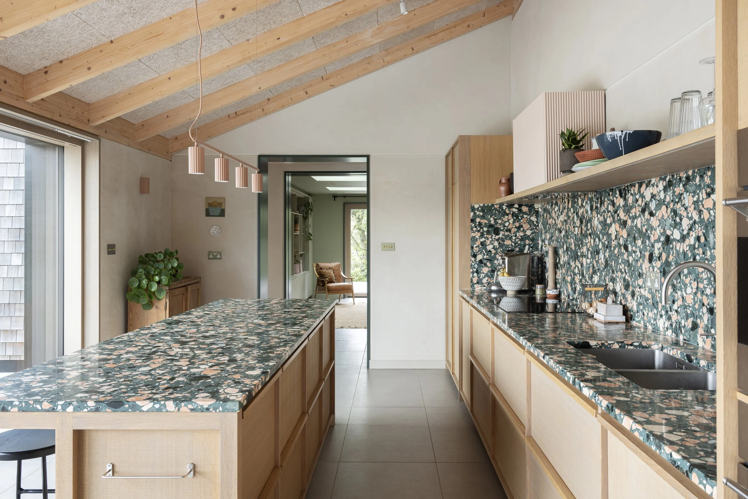 Modern kitchen with a terrazzo counter and backsplash, wooden cabinets, a sink, and an island with a matching terrazzo top.