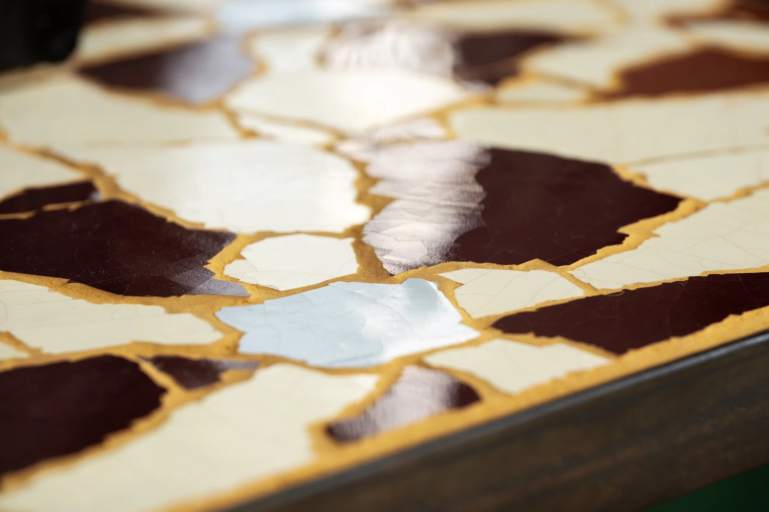 Close-up of a mosaic made of irregularly shaped tiles in shades of brown, cream, and light blue with a golden yellow grout.