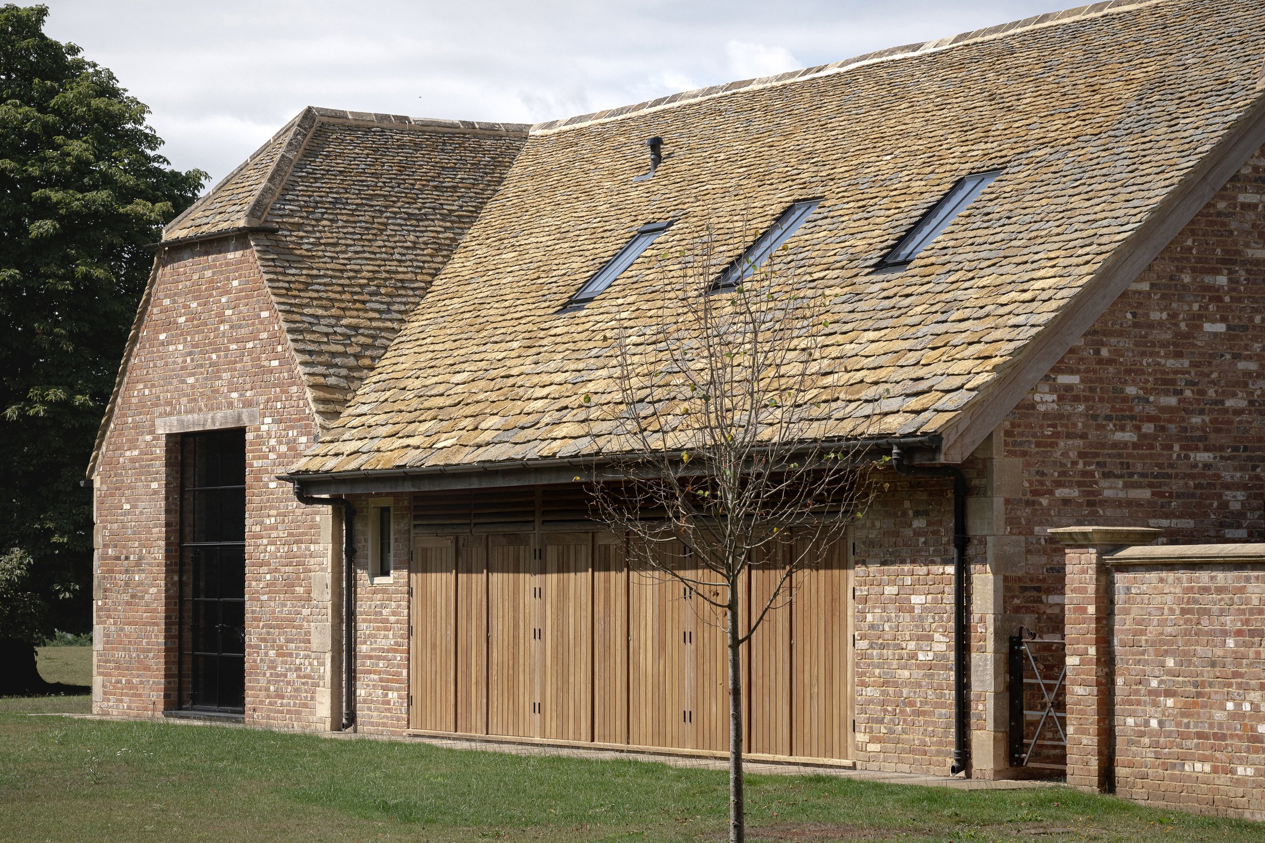 A brick house with a pitched shingle roof, three skylights, and a wooden garage door, with a small tree in front and a grassy yard.