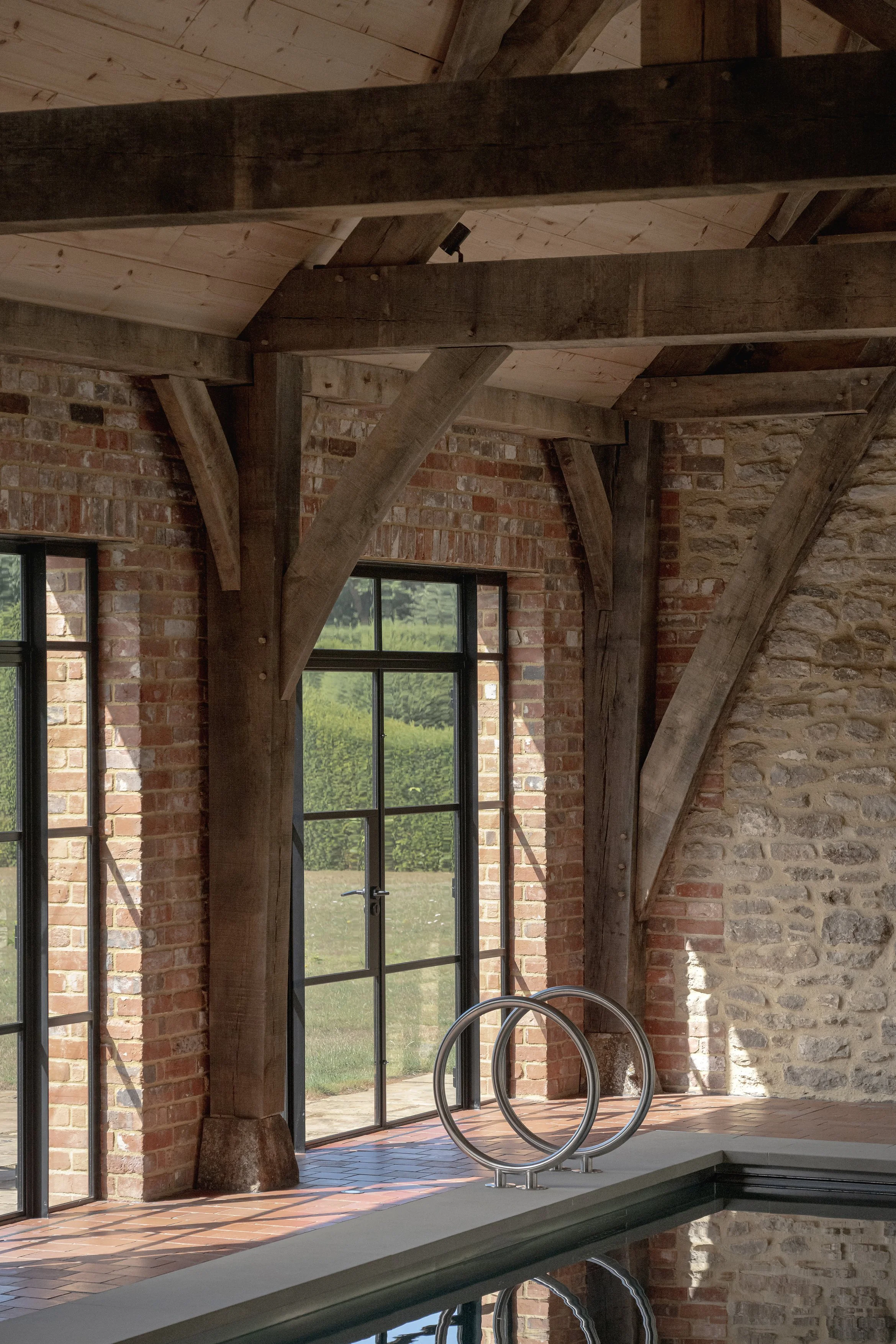 Indoor pool area with large glass doors, exposed brick and stone walls, wooden beams, and metal pool handrails.