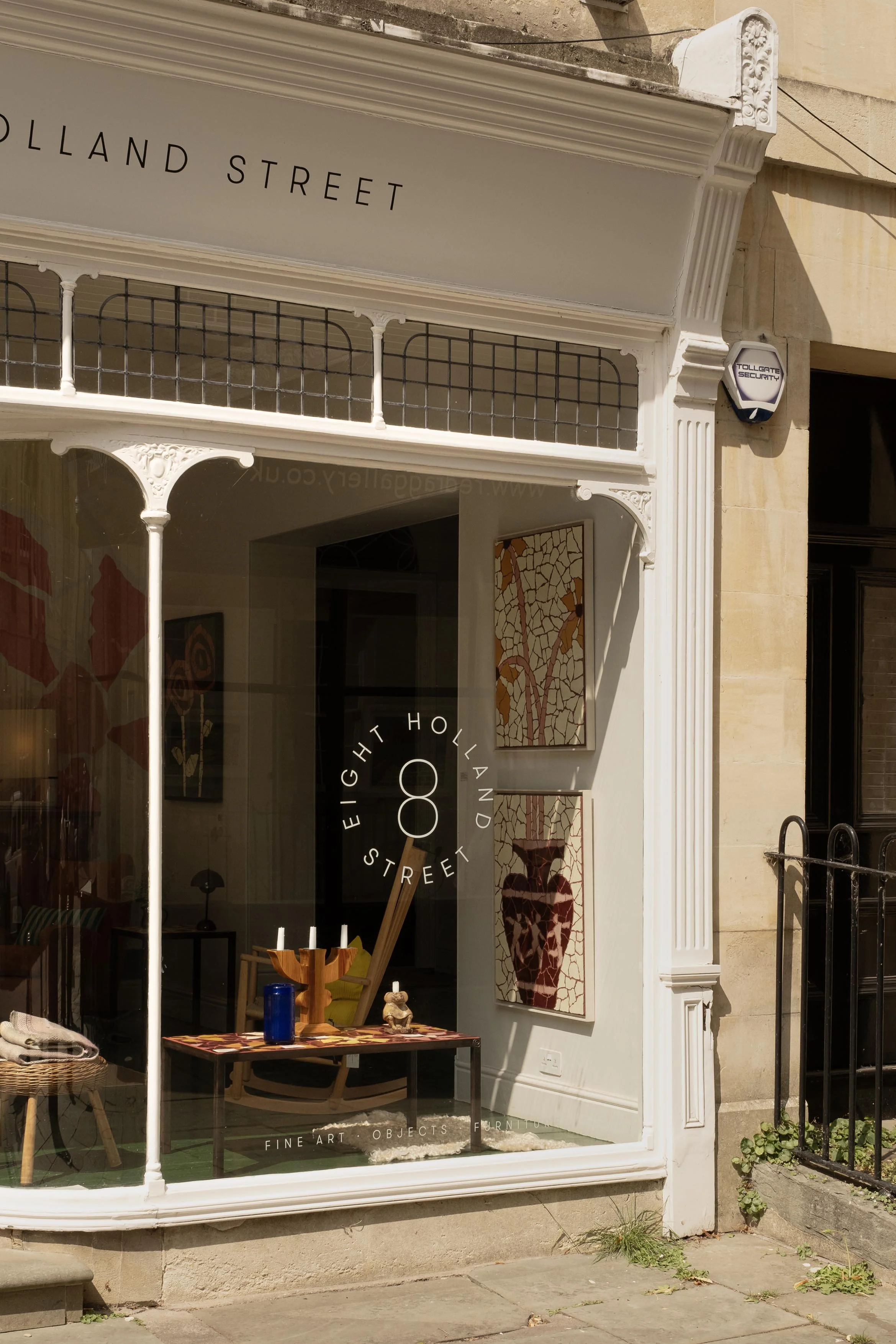 Storefront window with art pieces, including a painting of a vase with a cracked design, and a table with candles and decorative objects.