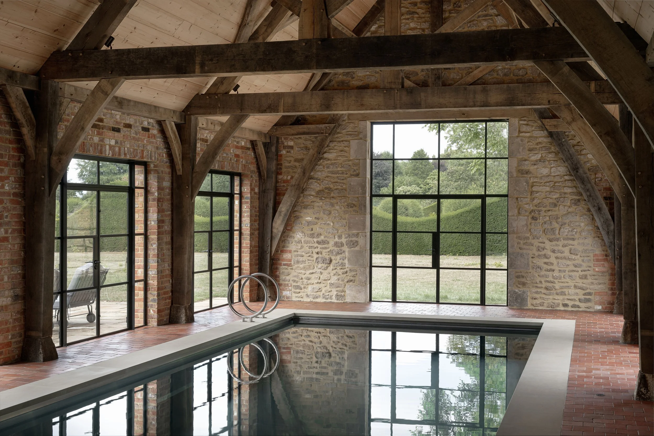 Indoor pool with brick and stone walls, large windows, and wooden beams on the ceiling.