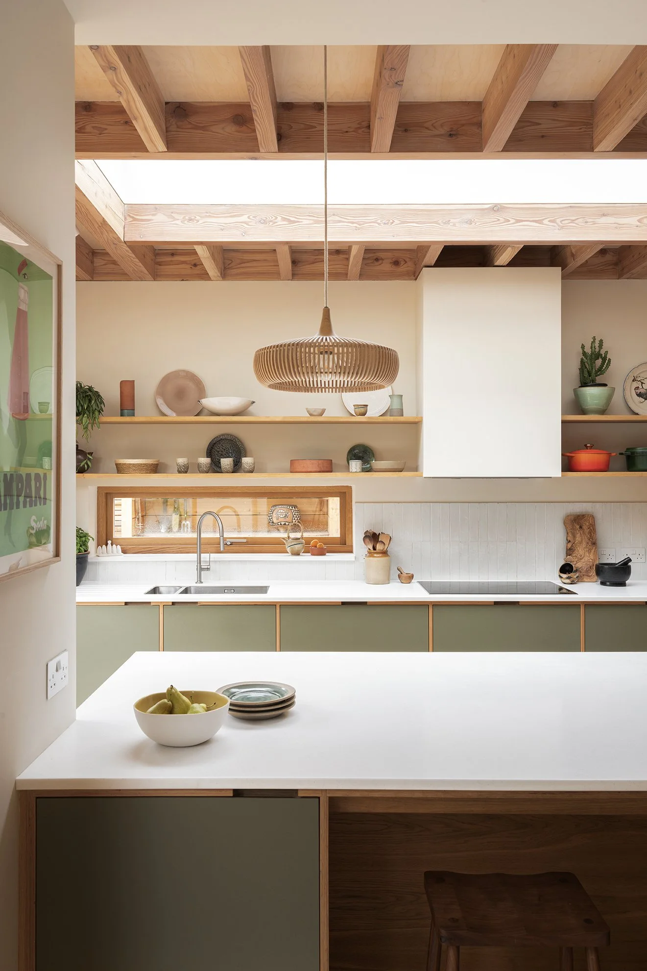 Modern kitchen with open shelving, green cabinets, wooden accents, and decorative dishes and plants.