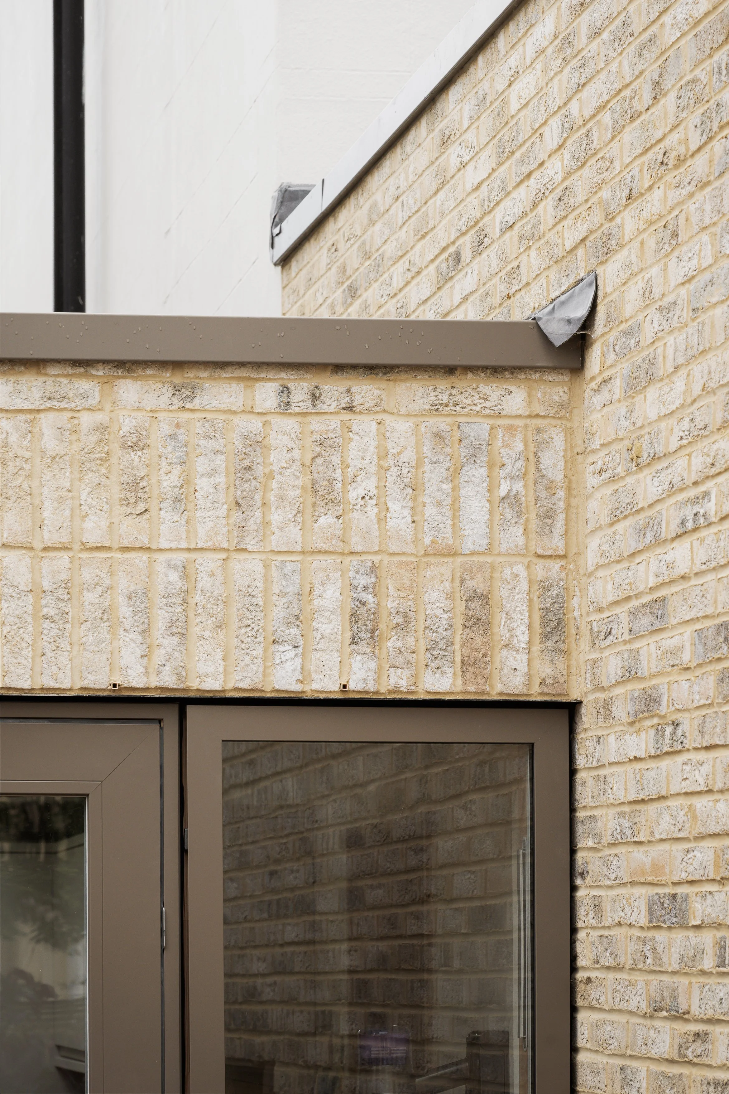 Close-up of building exterior showing brick wall, metal frame, and taped areas on the corner
