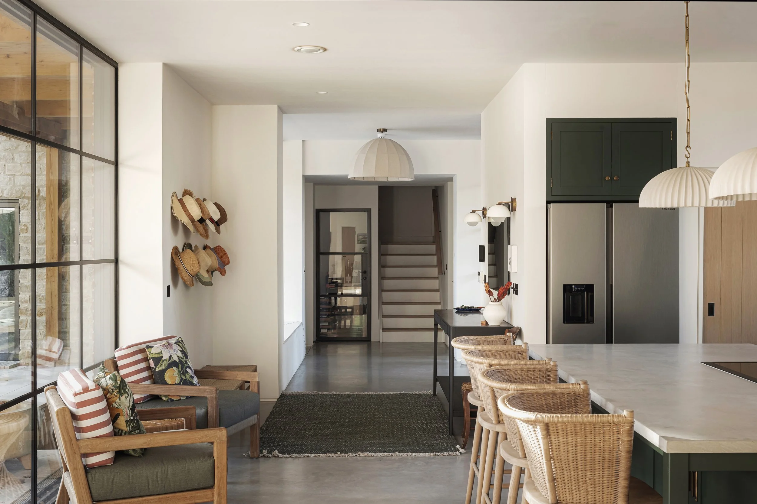 Modern kitchen and seating area with barstools, wicker chairs, and decorative hats on the wall leading to a staircase.