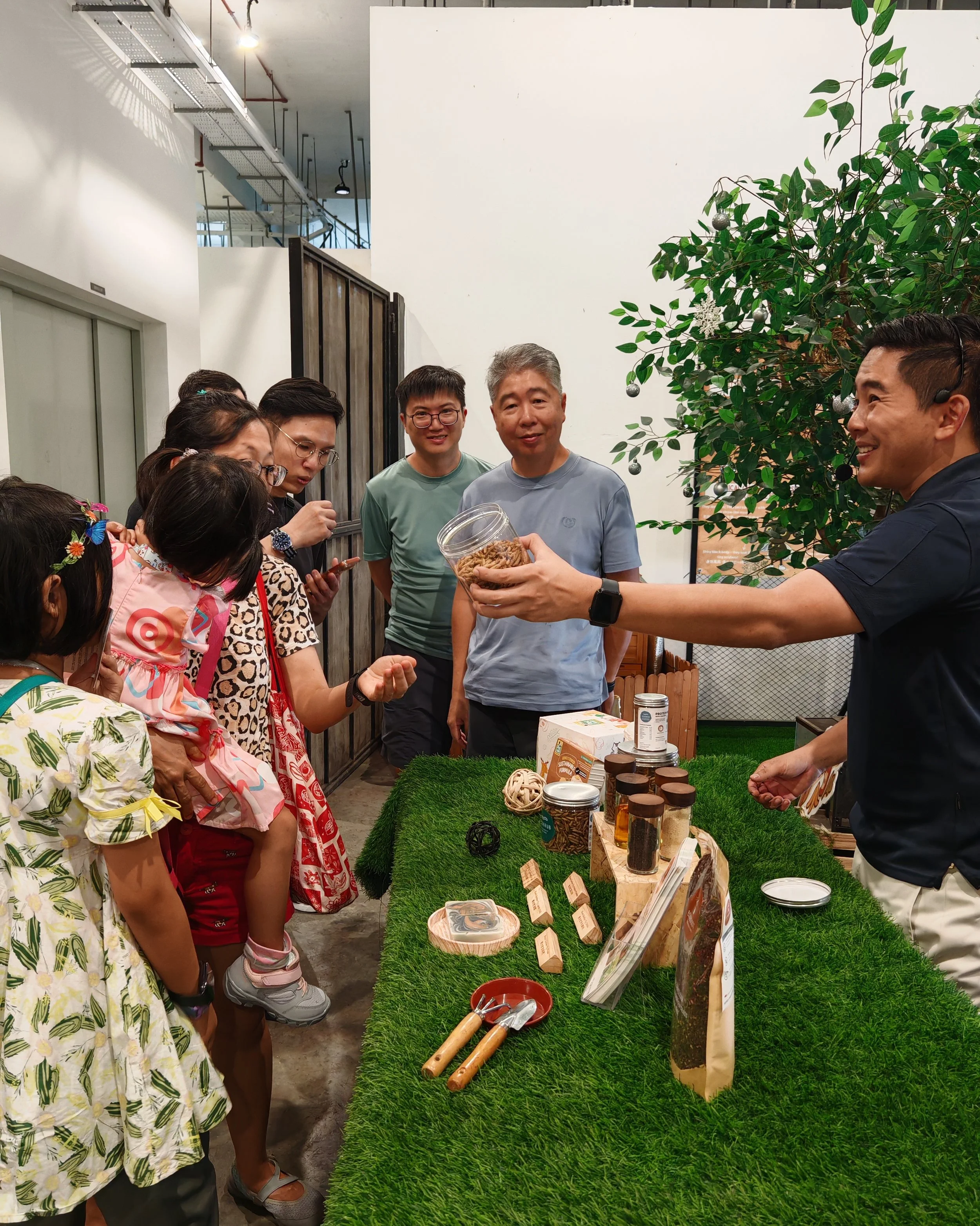 Group of people gathered Ento Industries' Display Booth during their Site Tour. They are tasting Ento Industries' Dried Black Soldier Fly Larvae