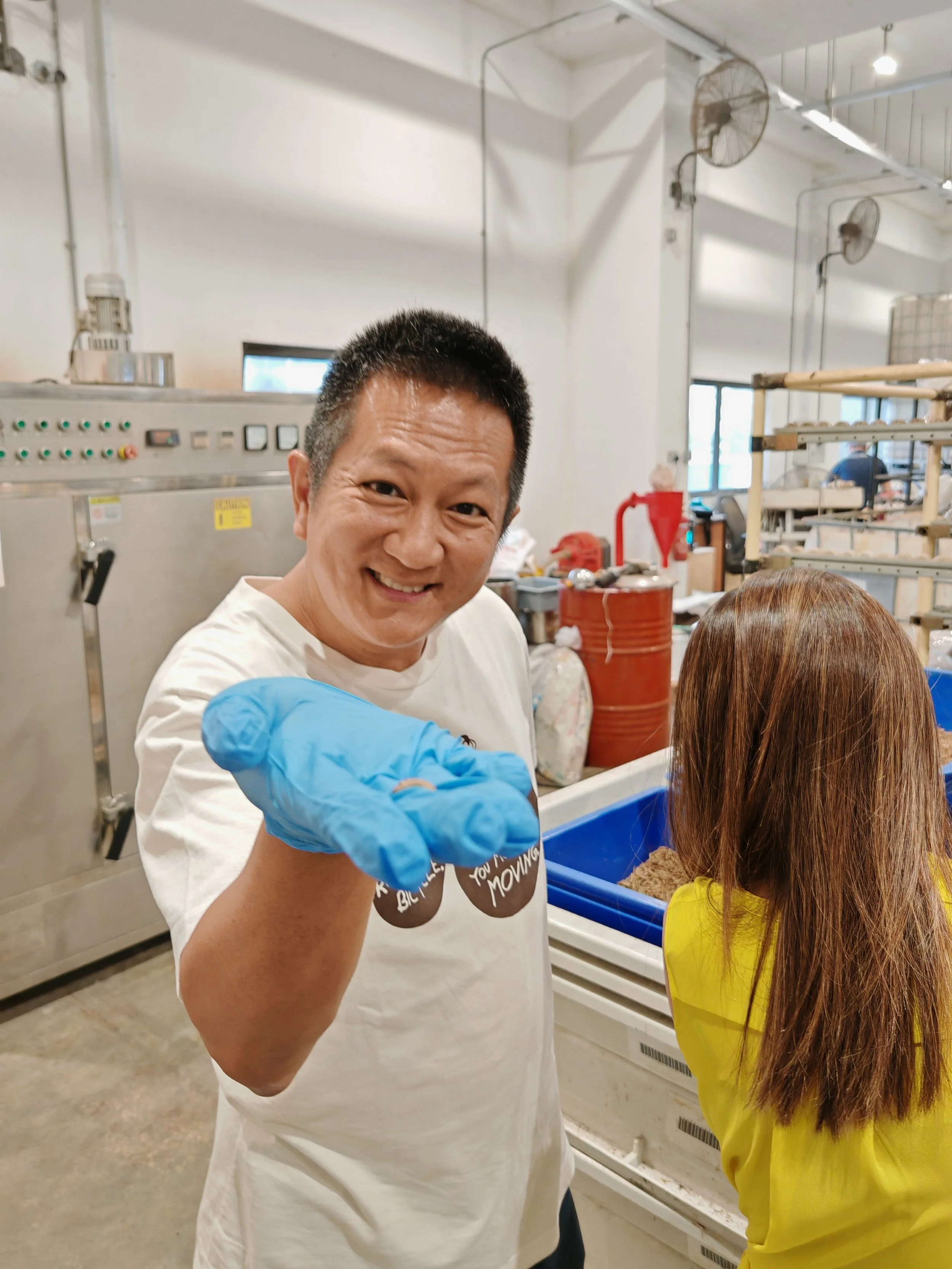 Ento Industries' Site Tour Participant Smiling Towards the Camera with a Live Black Soldier Fly Larvae In His Hand
