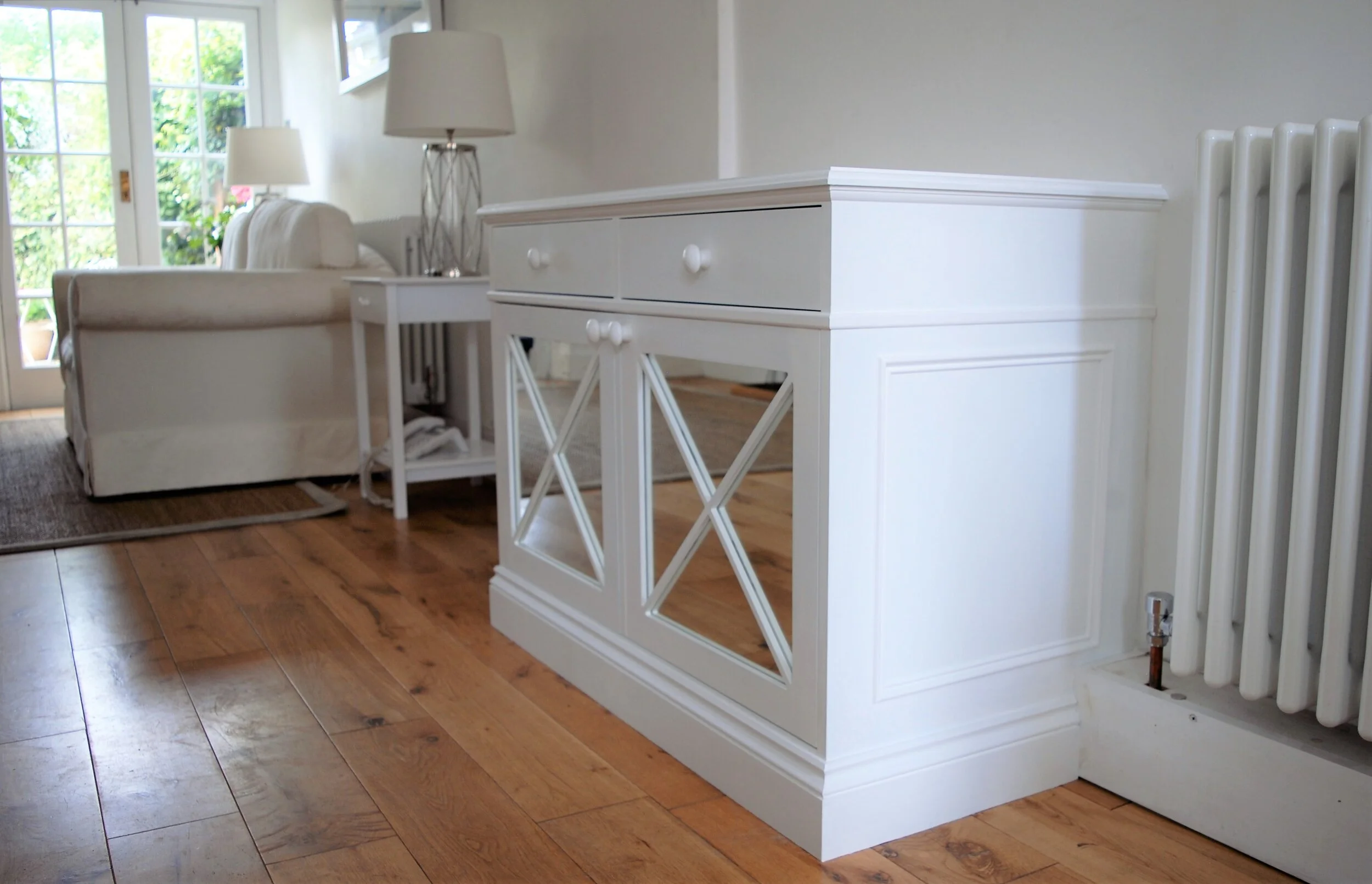 Living room with wooden floor, white furniture, and a sliding glass door leading outside, with sunlight coming in.
