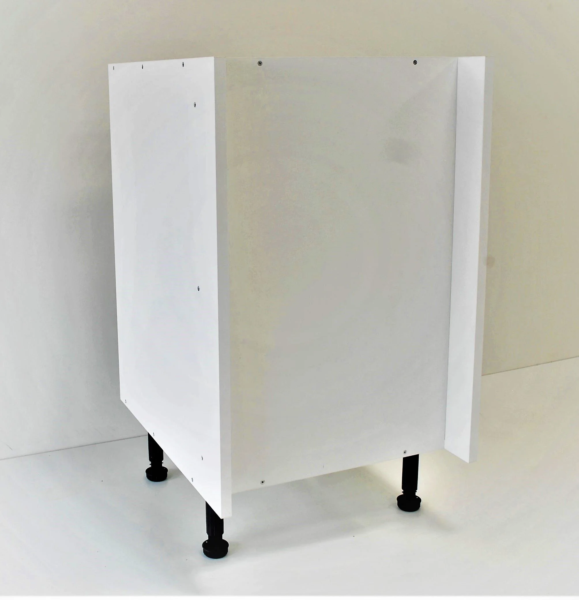 A white, box-shaped cabinet with black adjustable legs, placed against a plain wall.