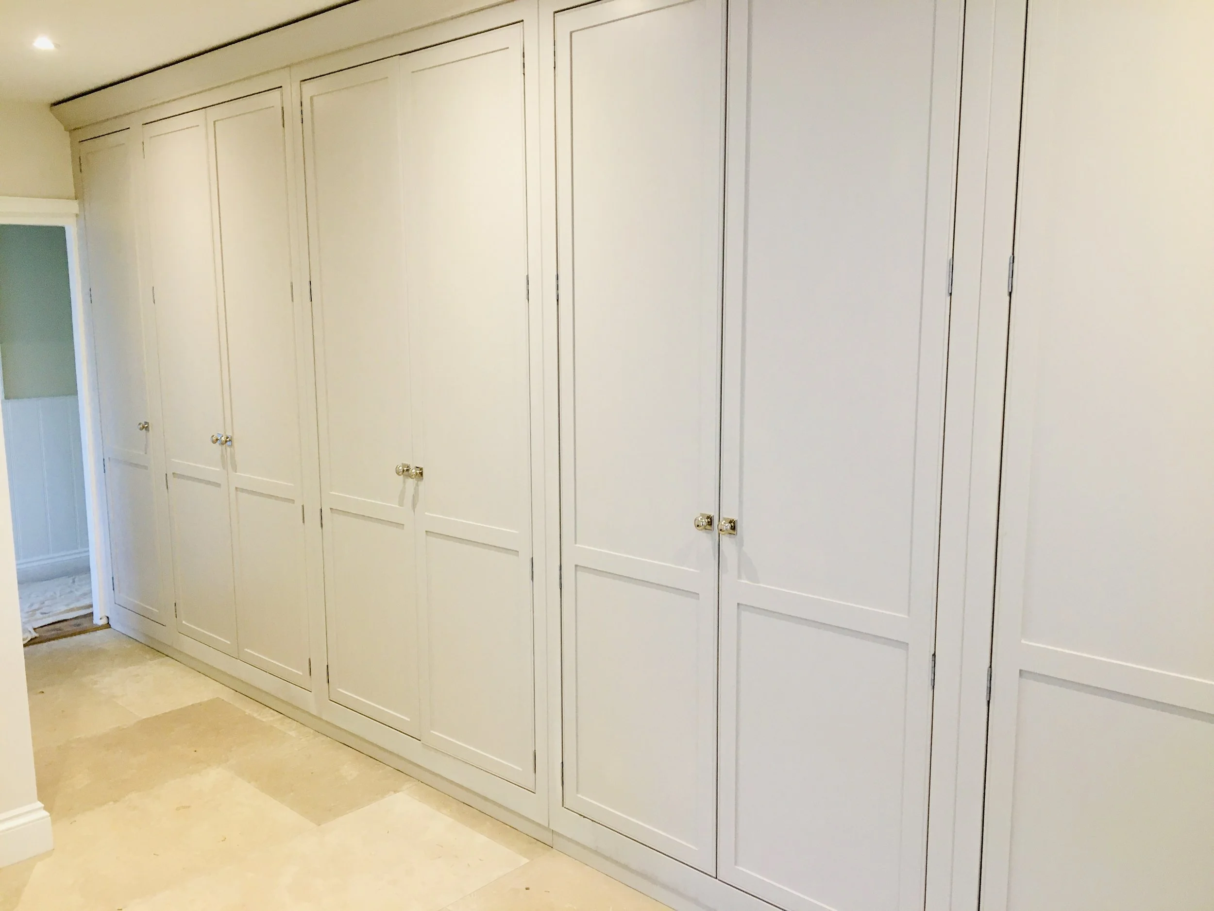 White built-in closet with multiple cabinet doors and brass knobs in a room with beige tiled floor.