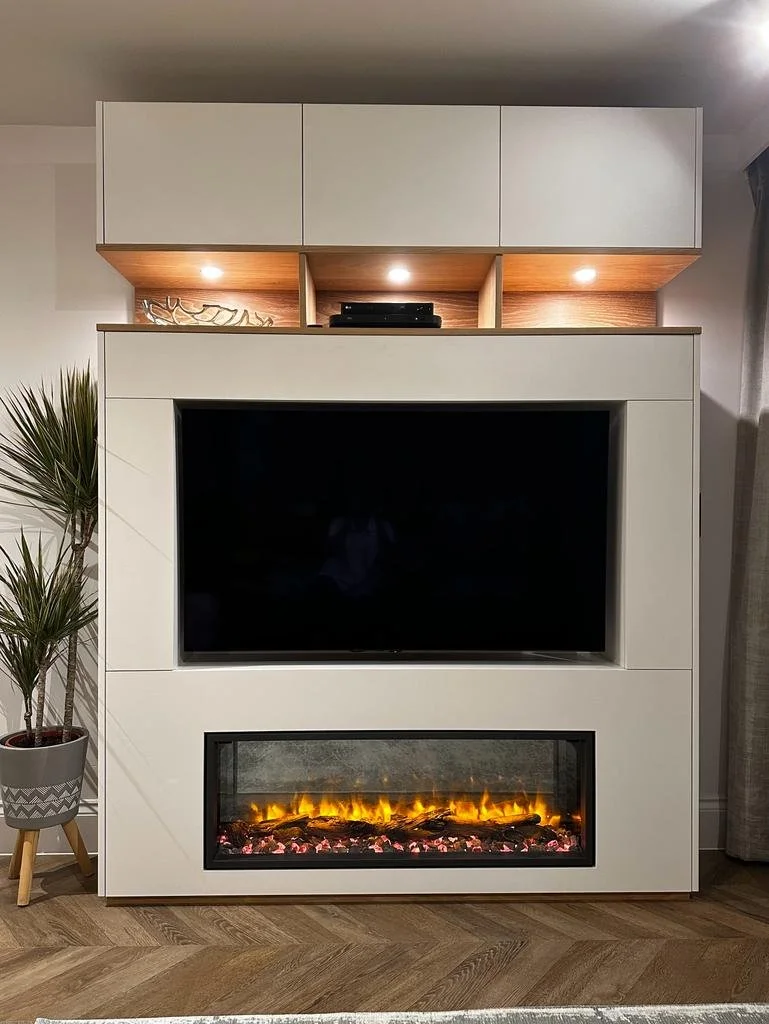 Modern entertainment center with a large flat-screen TV and an electric fireplace below, flanked by a potted plant on the left and gray curtains on the right.